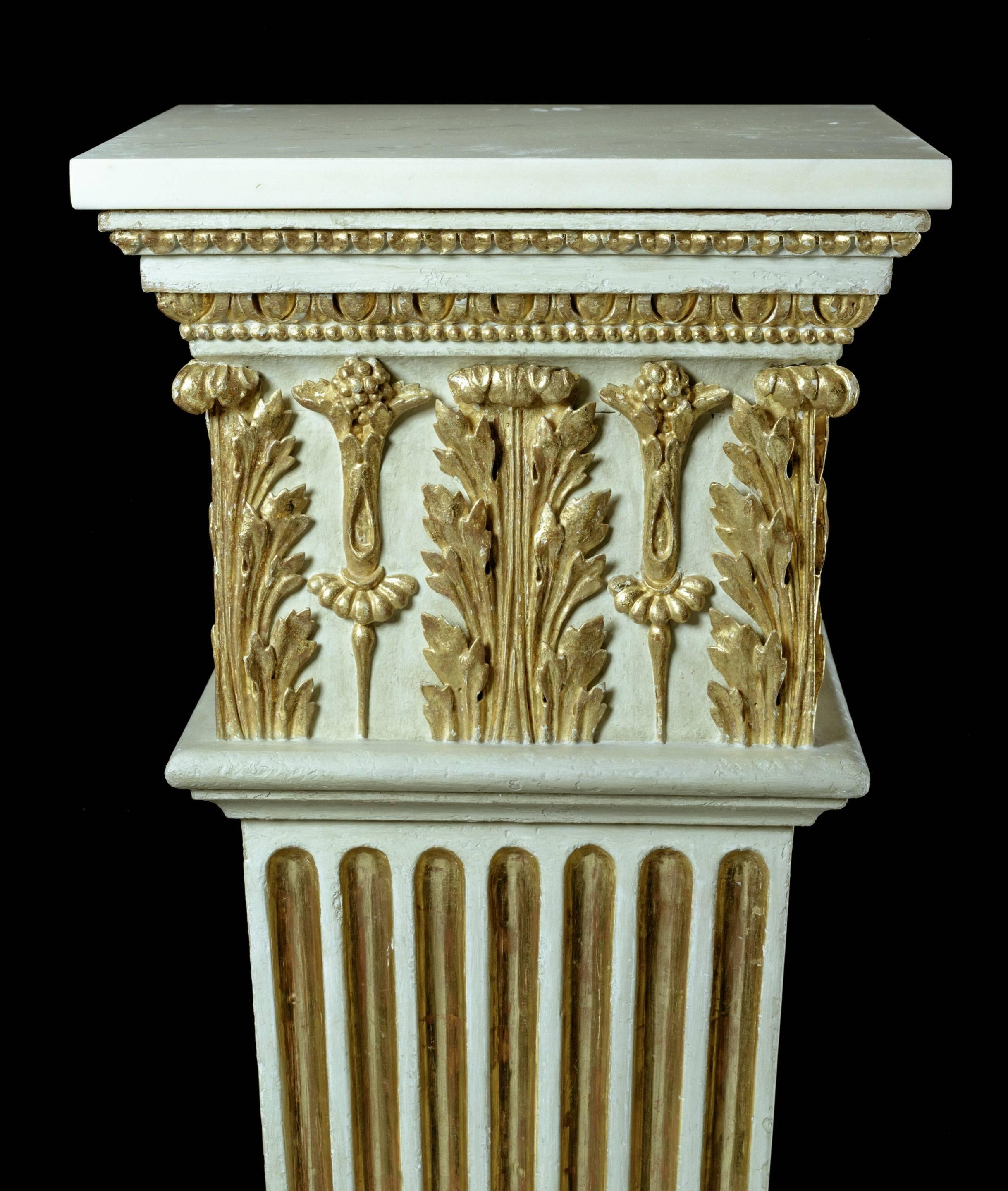 A fine pair of late 18th century white-painted and parcel gilt pedestals, the later square white marble tops on a beaded and egg and dart cornice above a carved acanthus frieze with square tapering fluted bodies on stepped block bases. 

It is