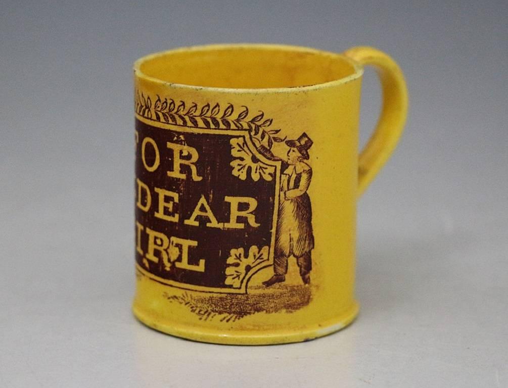 A charming canary yellow ground antique pottery mug with underglaze transfer print with a car-touche flanked by two male figures with the inscription 