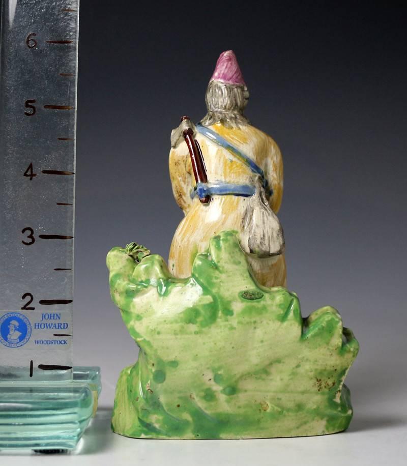 A fine Staffordshire pottery pearlware figure of Robinson Crusoe. The figure stands on a green base with a dead bird at his feet and a rifle propped again a green outcrop. He is carrying an axe and a bag on his back and wears a very sporting conical