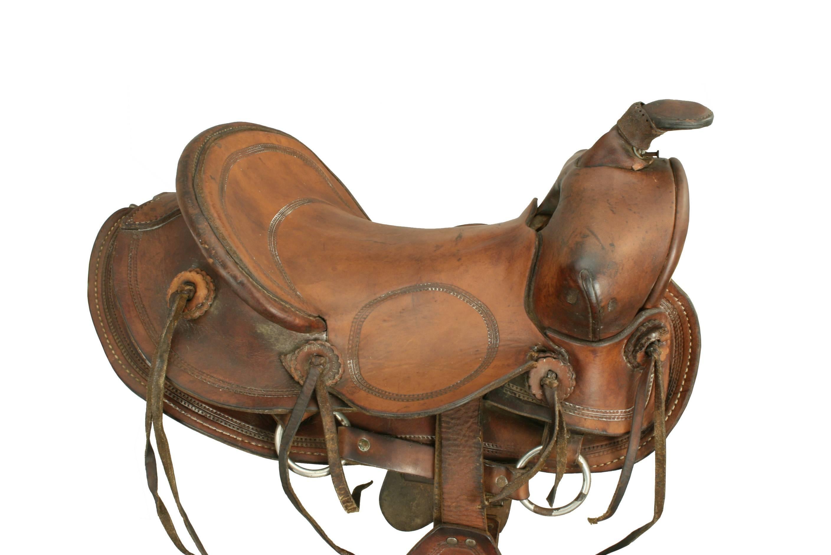 Vintage Child's Western Saddle.
A child's western saddle made from leather. The saddle comes with hooded safety stirrups and is decorated with some tooling on the seat, jockey and fender. The horn is a little lose from the pommel, the leather is a