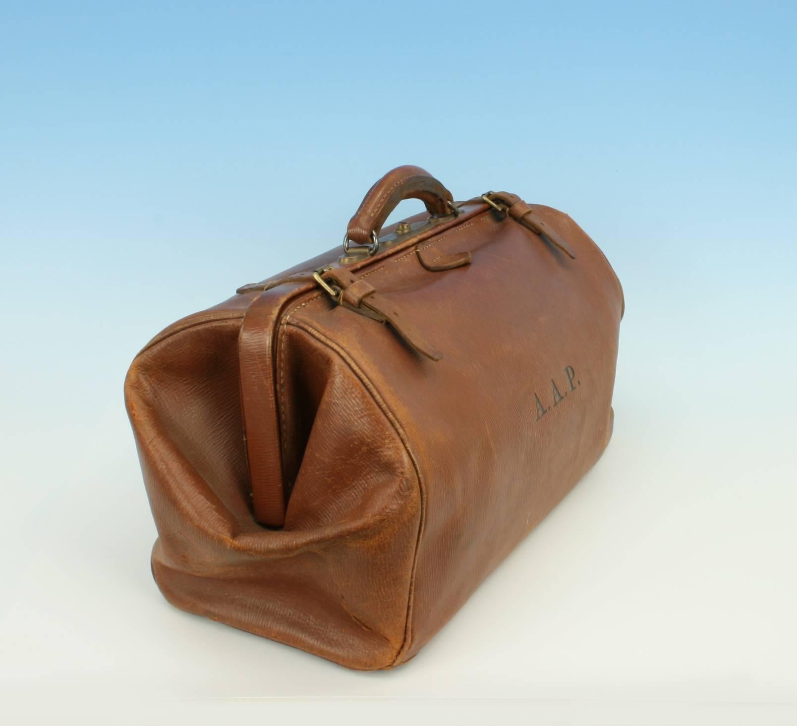 Vintage leather luggage, Gladstone bag, kit bag.
A traditional square mouth brown leather 'Gladstone' bag. The bag is fitted with four brass studded feet (one missing), a central push button lock, two leather straps and a single carry handle. The