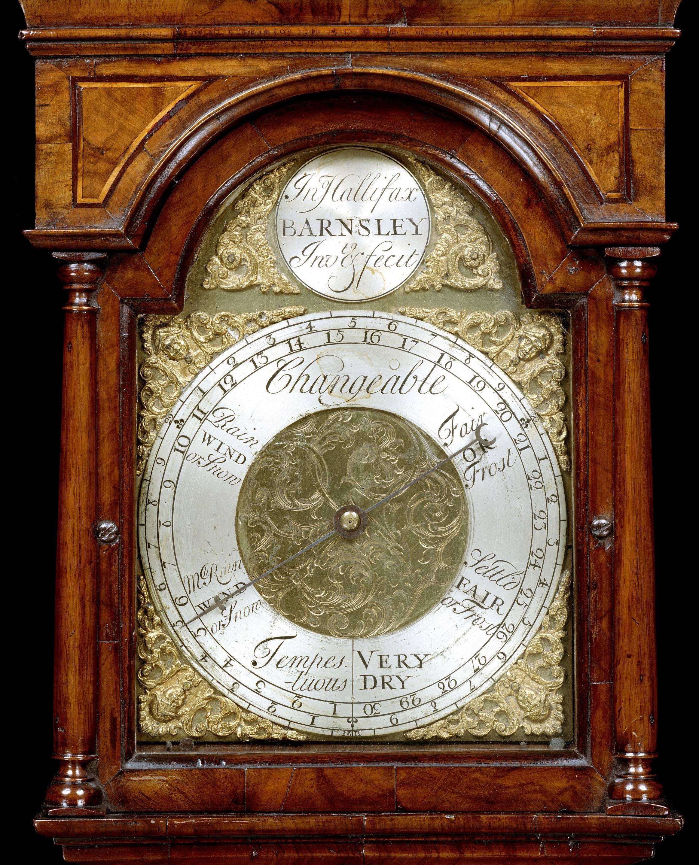 An extremely rare and important mid-18th century walnut barometer by John Hallifax of Barnsley, of distinctive long case clock shape, having a clock hood top with brass finials and glazed arched dial with a silvered chapter ring and brass spandrels