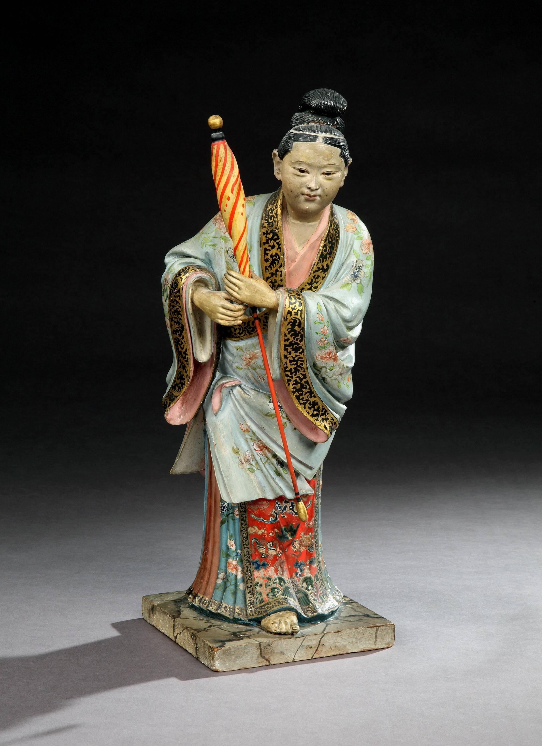 A pair of late 18th century polychrome painted Chinese export figures of a man and a lady wearing traditional Chinese dress, and retaining most of the original paint surface, the lady holding a folded umbrella; on plinth bases. 

Man: 
Height: