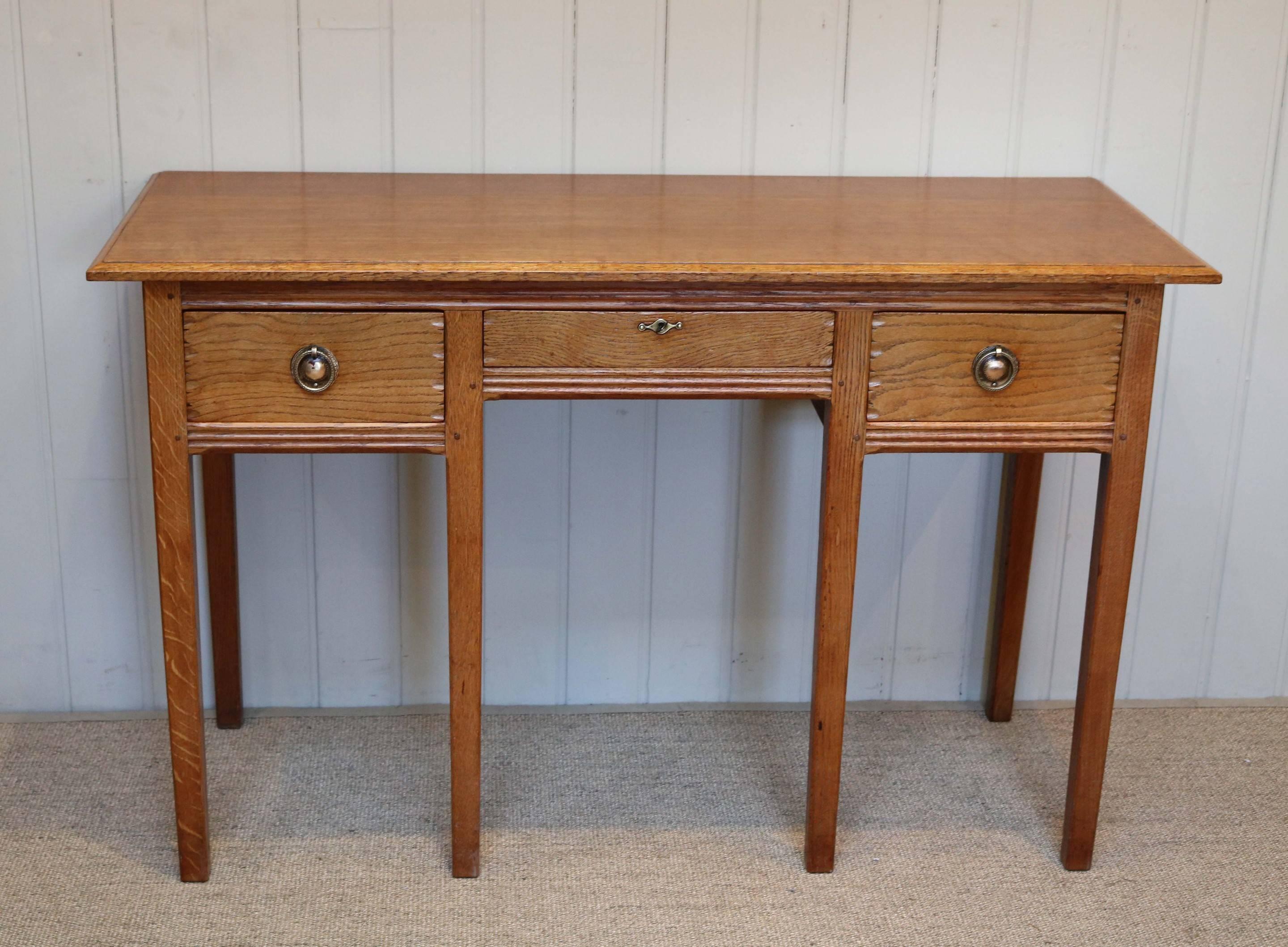 Original solid oak side or dressing table having three drawers with reeded edges and panelled sides raised on straight tapering legs. This piece of oak furniture was made in The Russell Workshops in Worcestershire the designer was Gordon Russell and