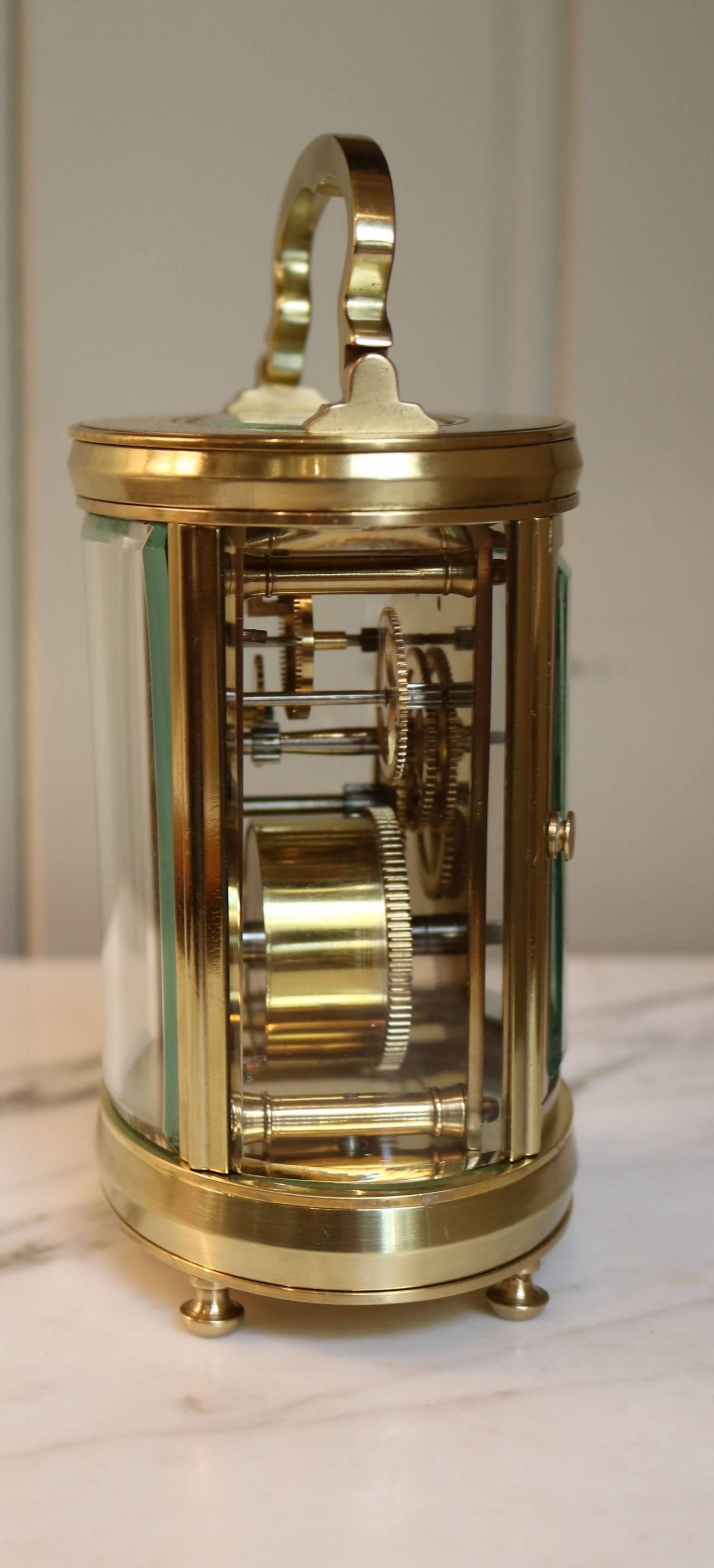A French brass carriage clock in the more unusual oval form. The brass case has a shaped top handle and bevel edge glass around and in the top window. It has an enamel dial and an 8 day timepiece movement with a cylinder platform. The backplate has