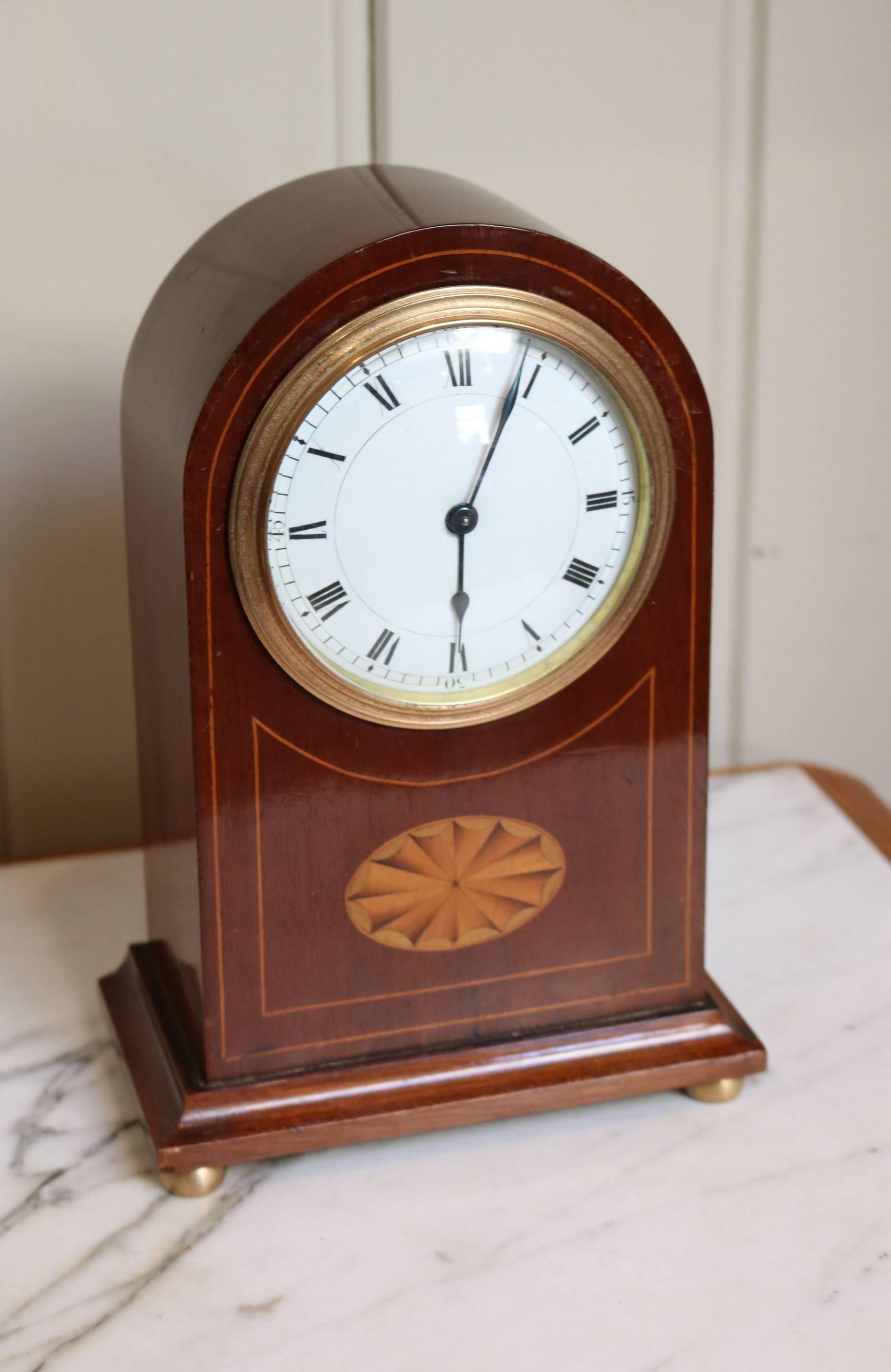 A solid mahogany mantel clock dating to the Edwardian period. It has a arch top and is inlaid with boxwood stringing a a satinwood fan motif. The convex enamel dial has Roman numerals with 15 minute markers. The Swiss 8 day movement has a cylinder