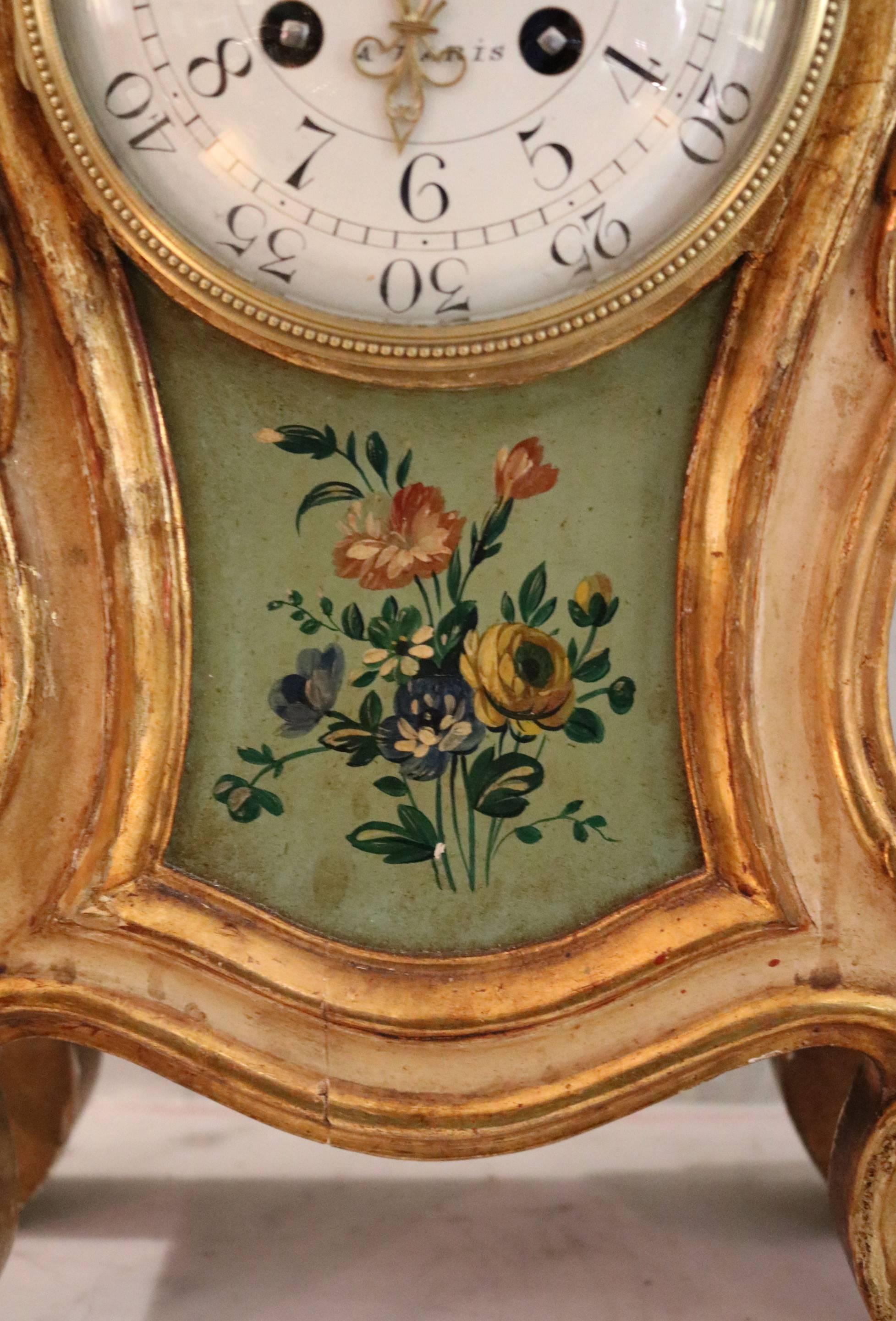 An imposing carved giltwood and painted mantel clock in the Louis XV style, made circa 1900. It has a waisted case, with a carved ribbon and acanthus swag above the dial, and a painted floral panel below with matching sides. The enamel dial has a