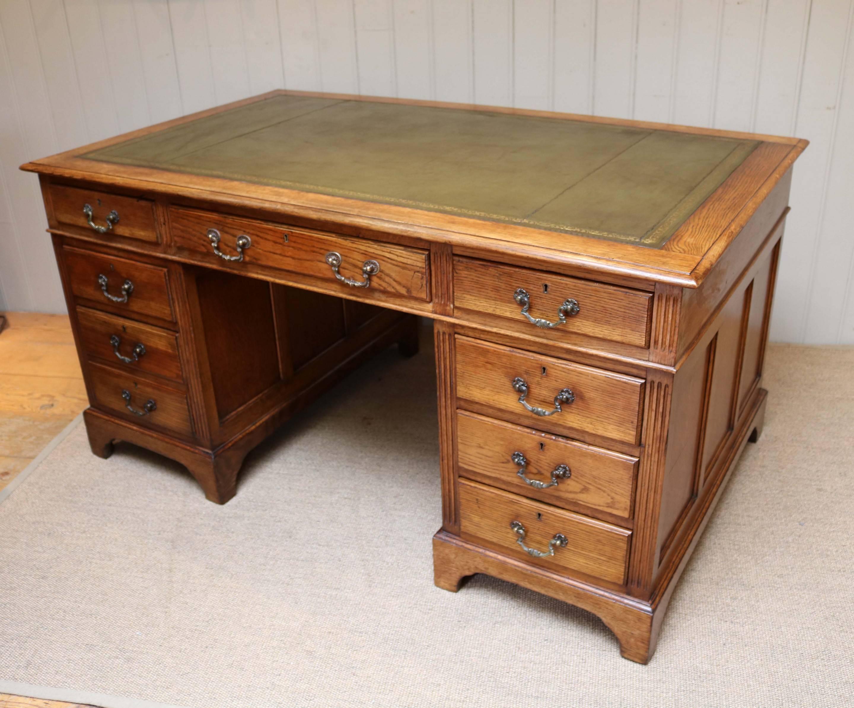 Large oak pedestal desk having a green tooled leather top above three drawers with a further three drawers to one side and two to the other having reeded edges and paneled sides.
