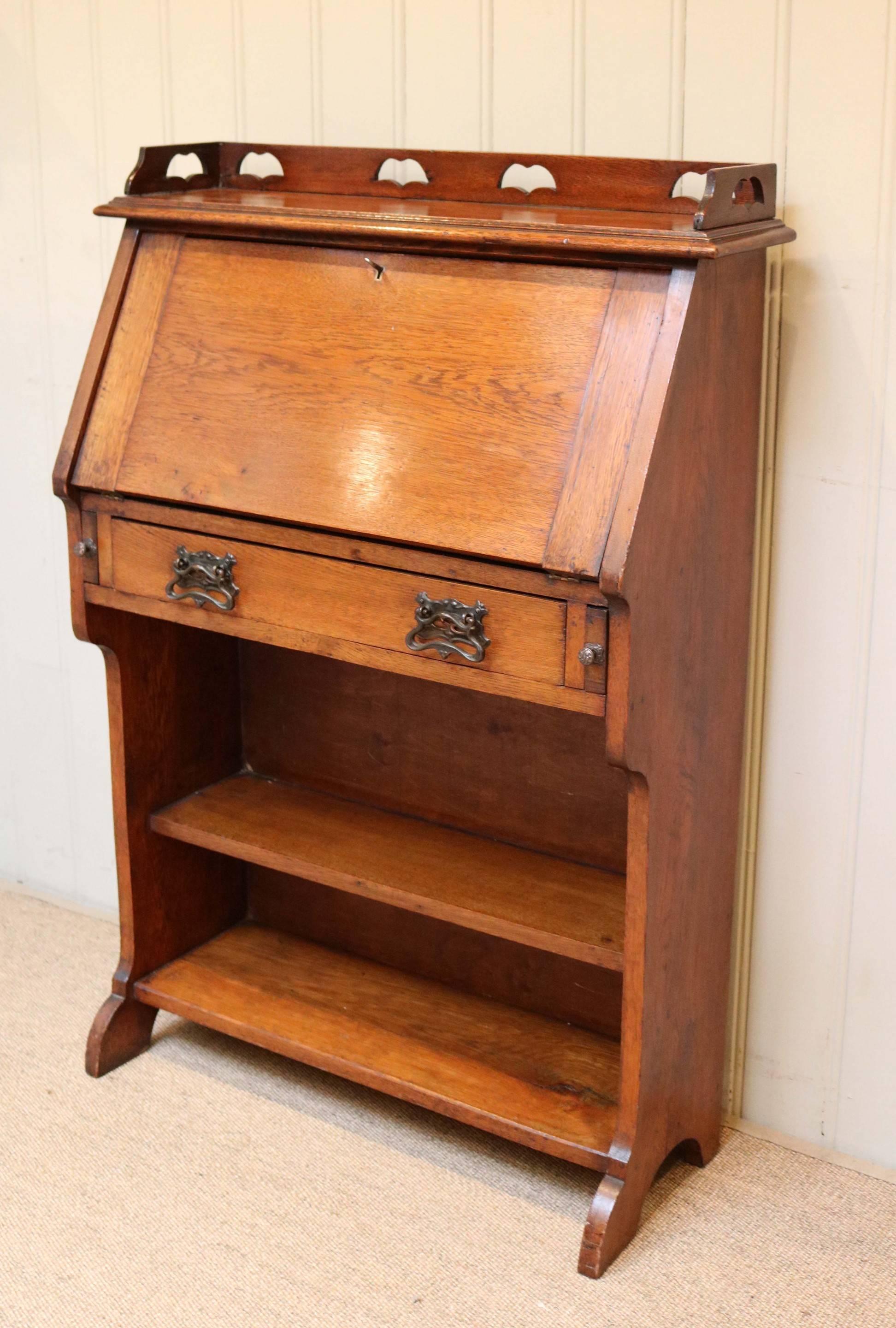 Oak arts and crafts bureau having a fall front which opens to reveal a fitted interior above a single drawer and open bookcase base.