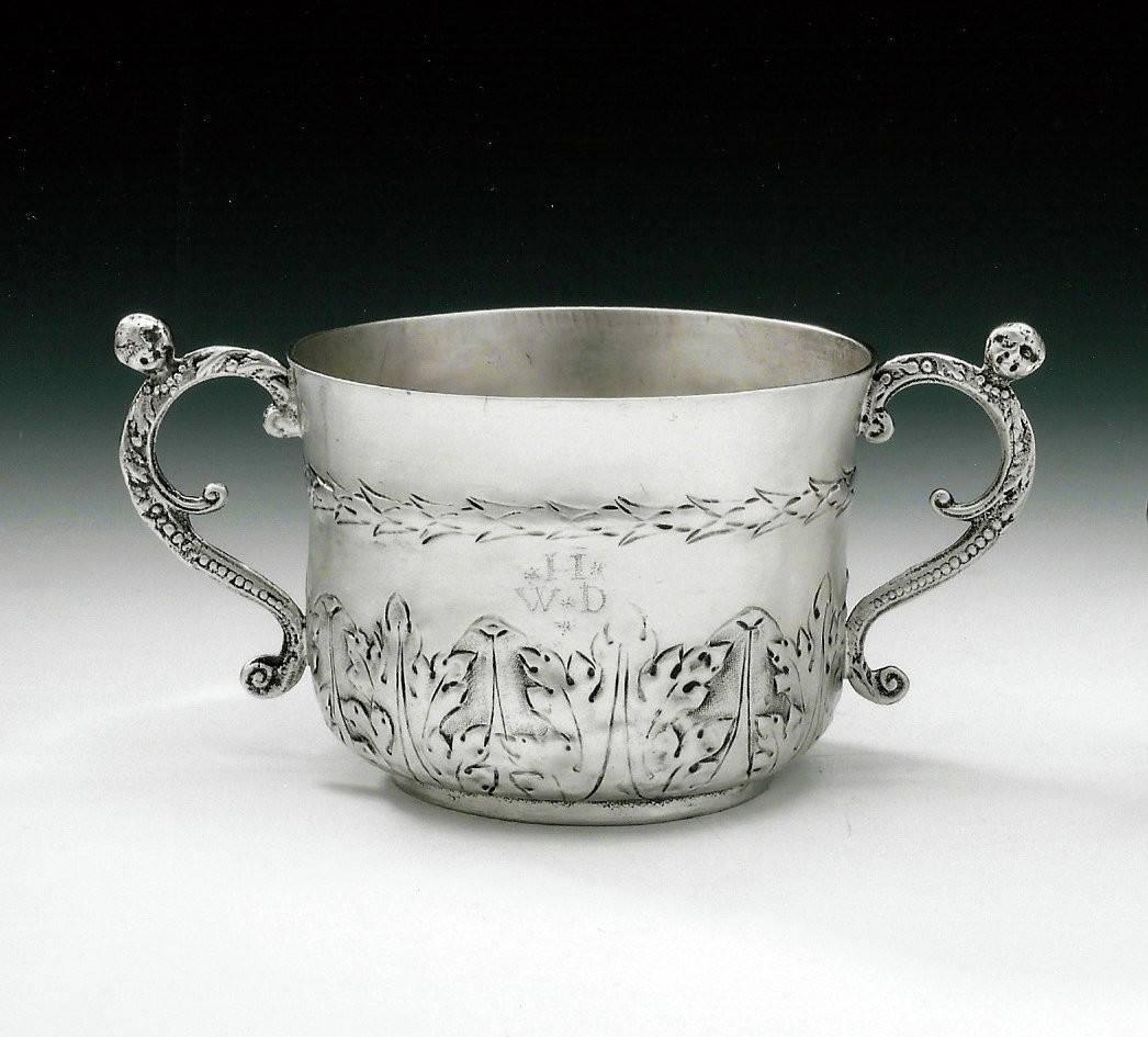 The Porringer is of typical form for this date and is decorated, on the lower section of the main body, with acanthus and palm leaf motifs. The upper section displays a band of stylised arrow head motifs and two cast scroll and bead handles with