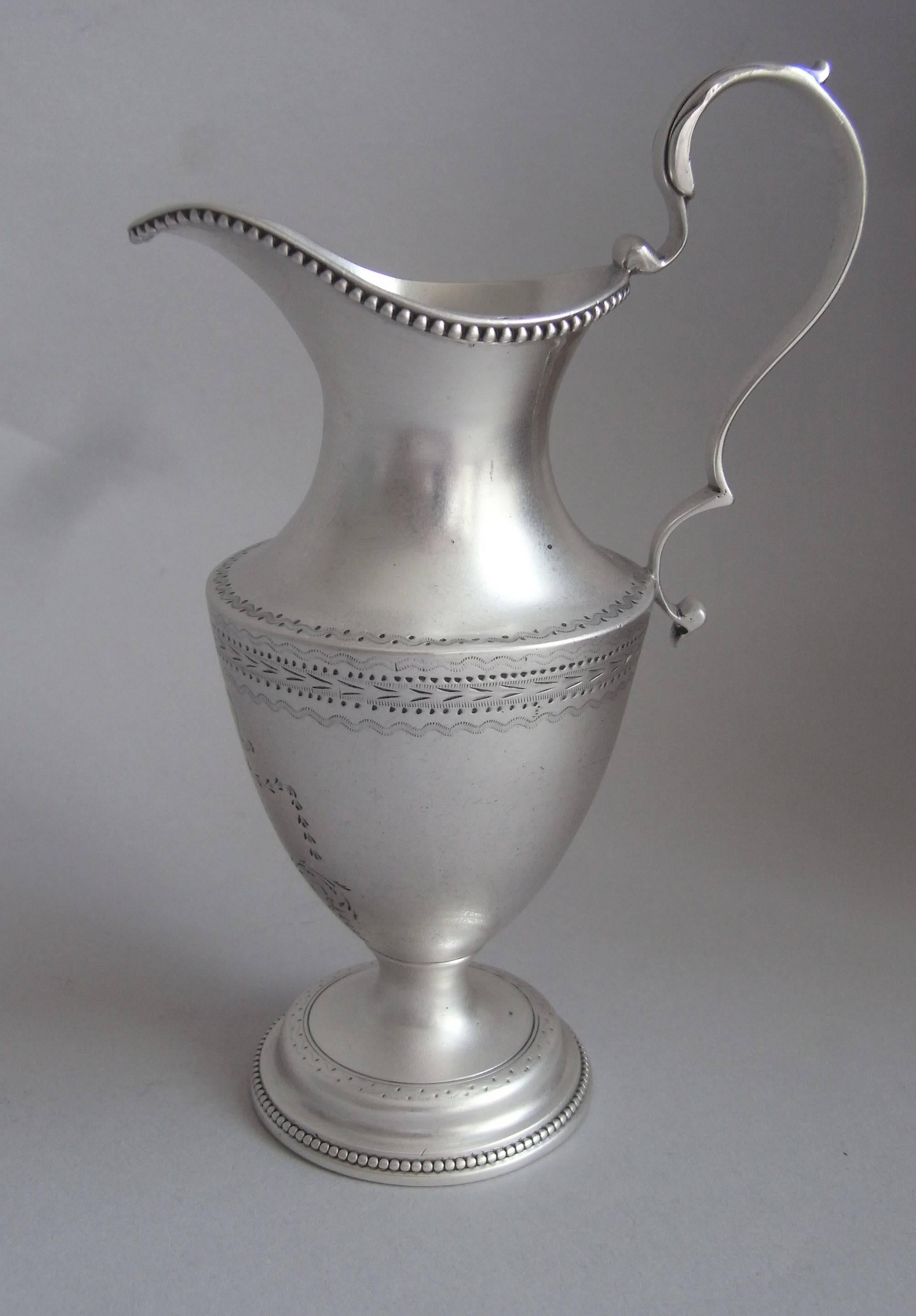 The jug is modelled as a neoclassical Ewer and stands on a stepped circular foot which is decorated with beading and prick dot designs. The vase shaped main body is also engraved with prick dot and bright cut bands. The front displays an oval