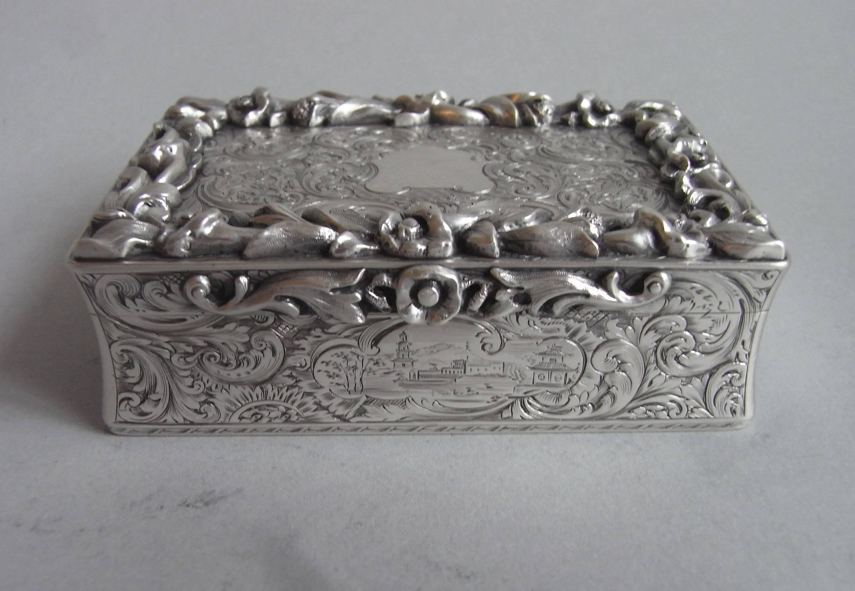 The snuff box is of broad rectangular form and has slightly incuse corners. The cover displays an outer cast raised border of trailing foliage and flower heads in bloom. This border encloses an exceptionally engraved panel of pluming scrolls and