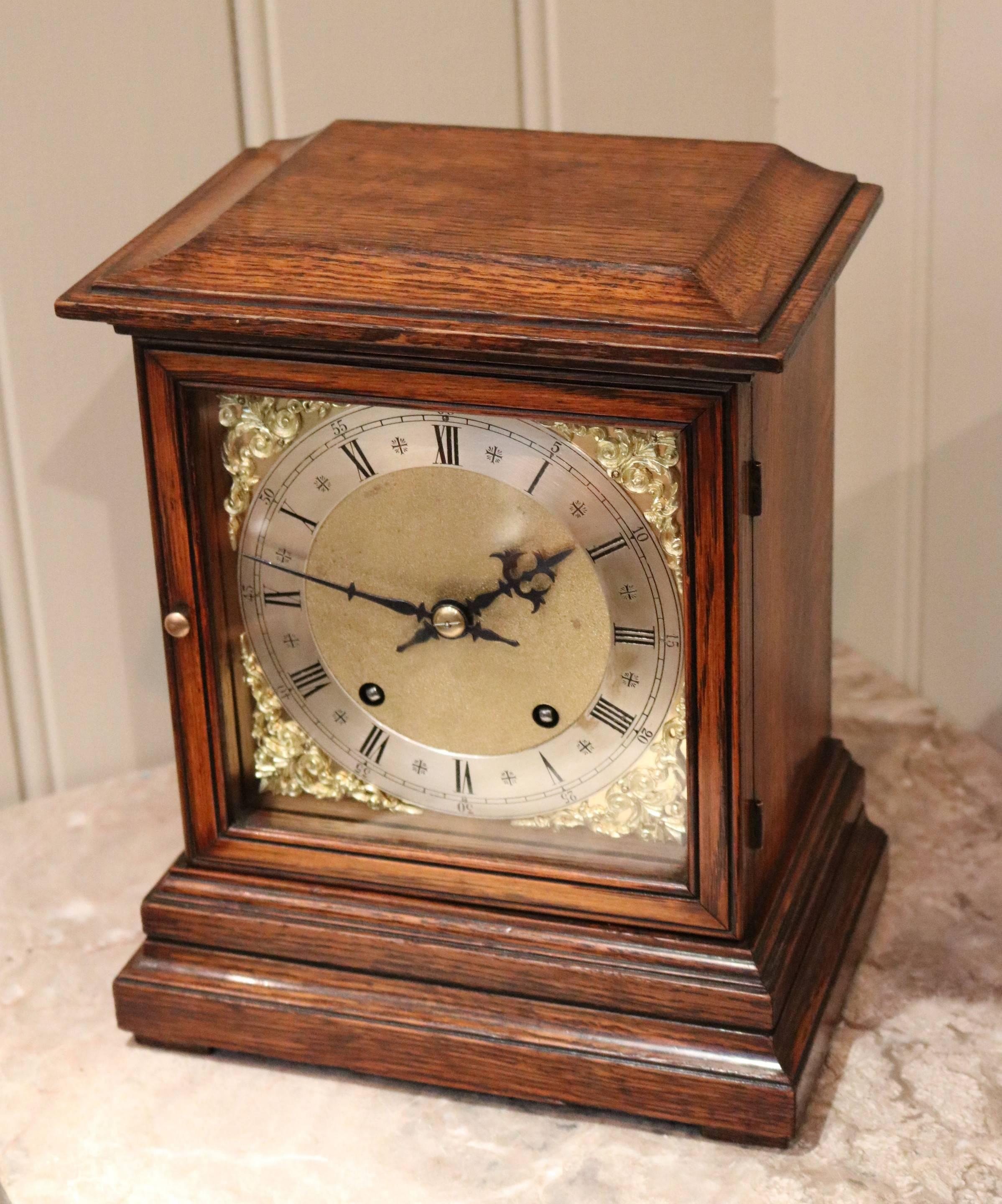 An oak mantel clock dating to the late Victorian period, from around the end of the 19th century. It has a solid oak case of simple form, with a brass dial, silvered chapter ring and brass corner spandrels. It has an 8 day movement that strikes the