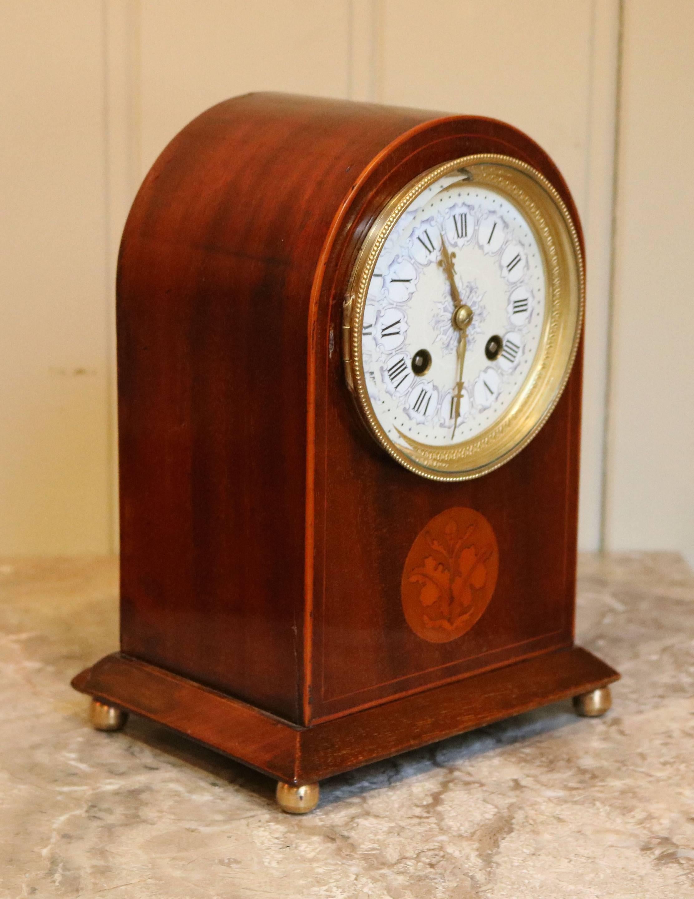 A French mahogany arch top mantel clock with boxwood stringing and inlay to the front and chamfered base. The clock is raised on four brass ball feet and has an embossed brass bezel with a flat bevel edged glass and an unusual ornate cream and blue