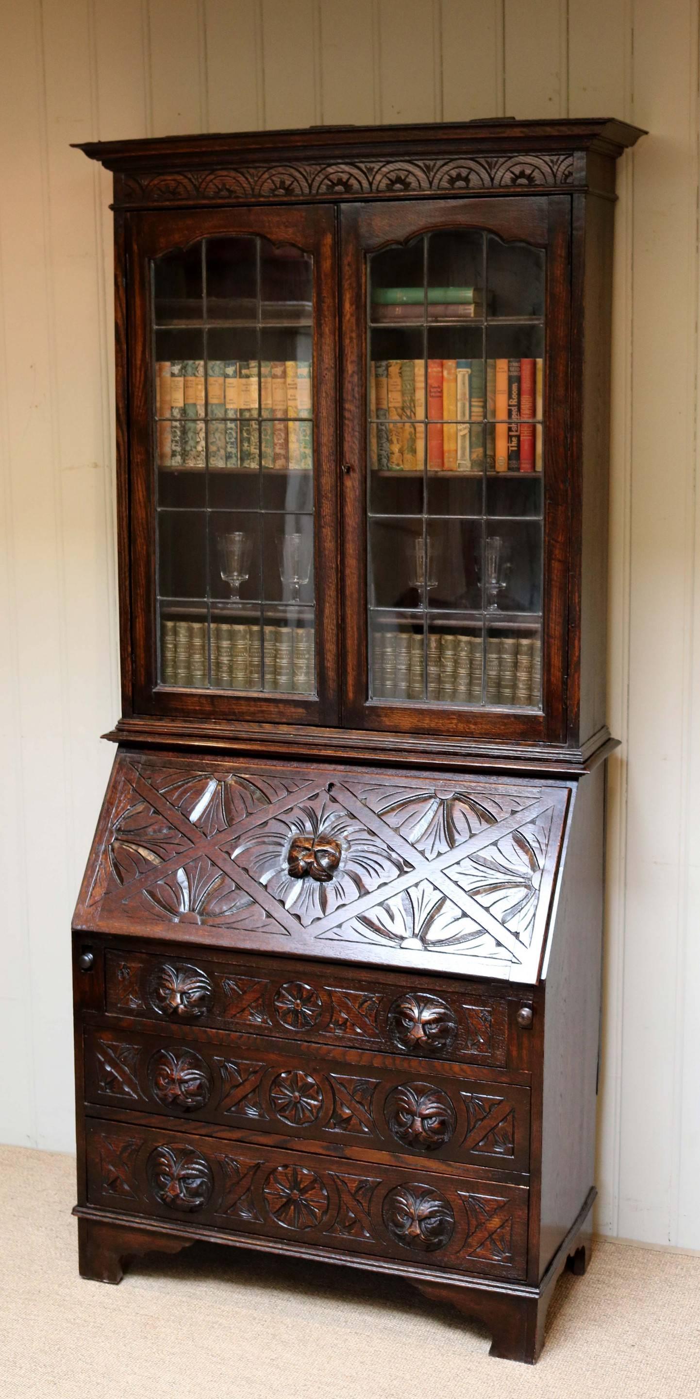 Carved oak green man bureau bookcase having a two door lead light glazed top with three fixed internal shelves, above a bureau base comprising of three drawers below a carved fall front opening to reveal a fitted interior.