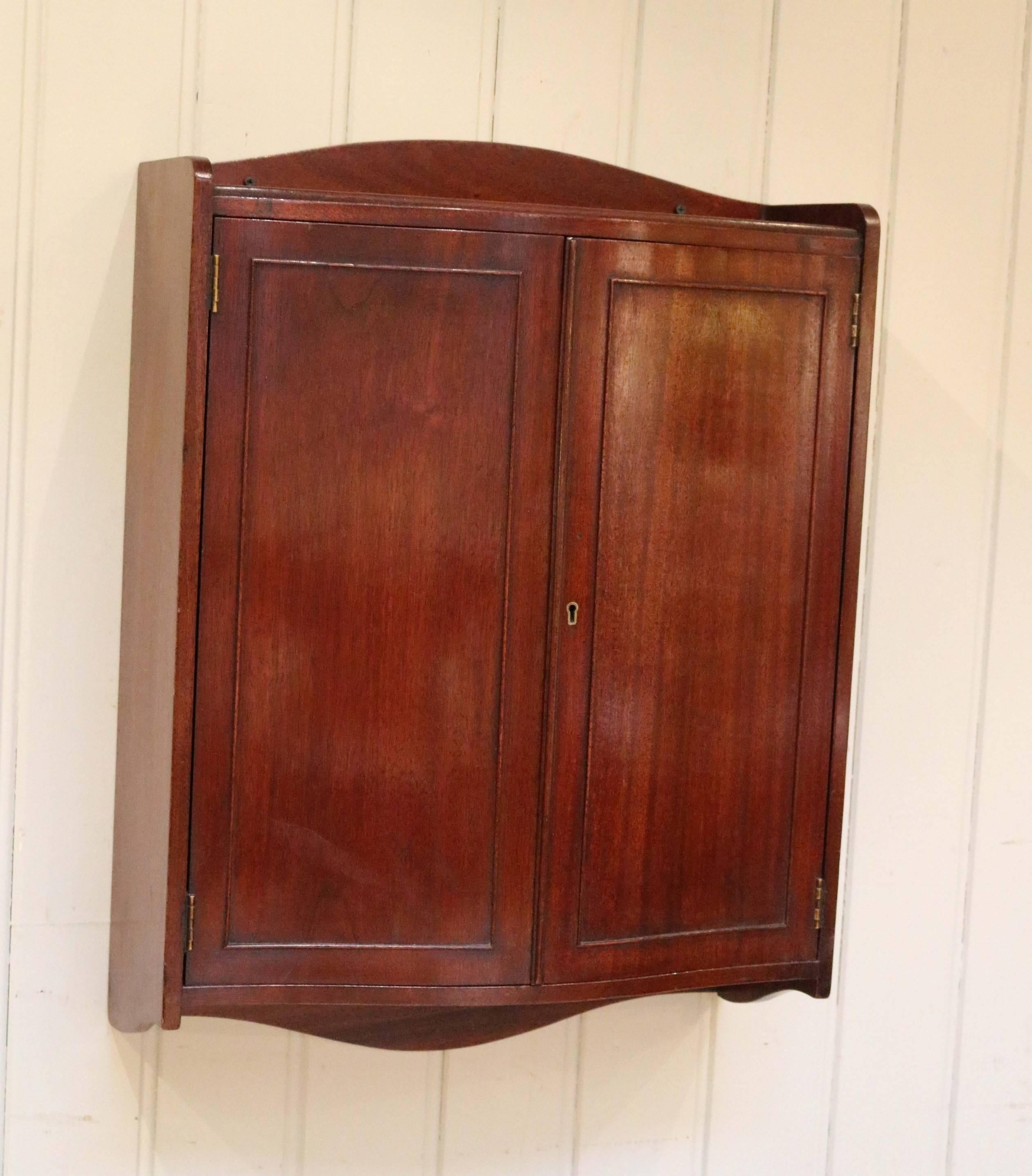 Edwardian mahogany two-door wall cabinet having a serpentine front with a fixed internal shelf.