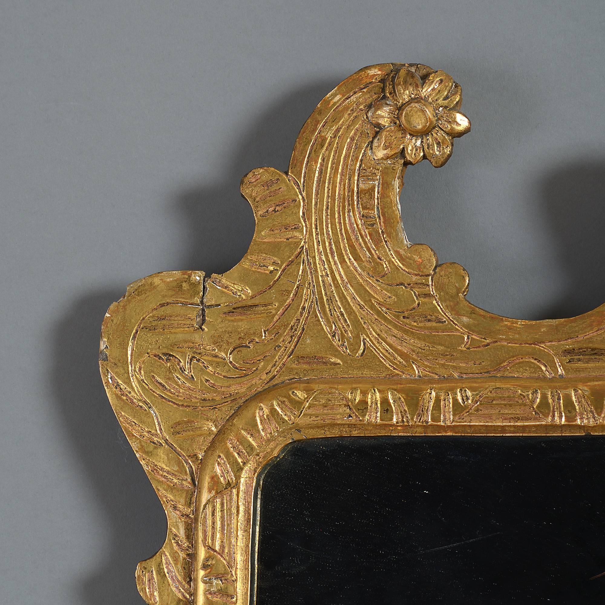 A George I style giltwood mirror, having a scrolling cresting with flower heads, applied swags to the sides and a shaped scrolling apron. 

Retaining early 18th century elements.