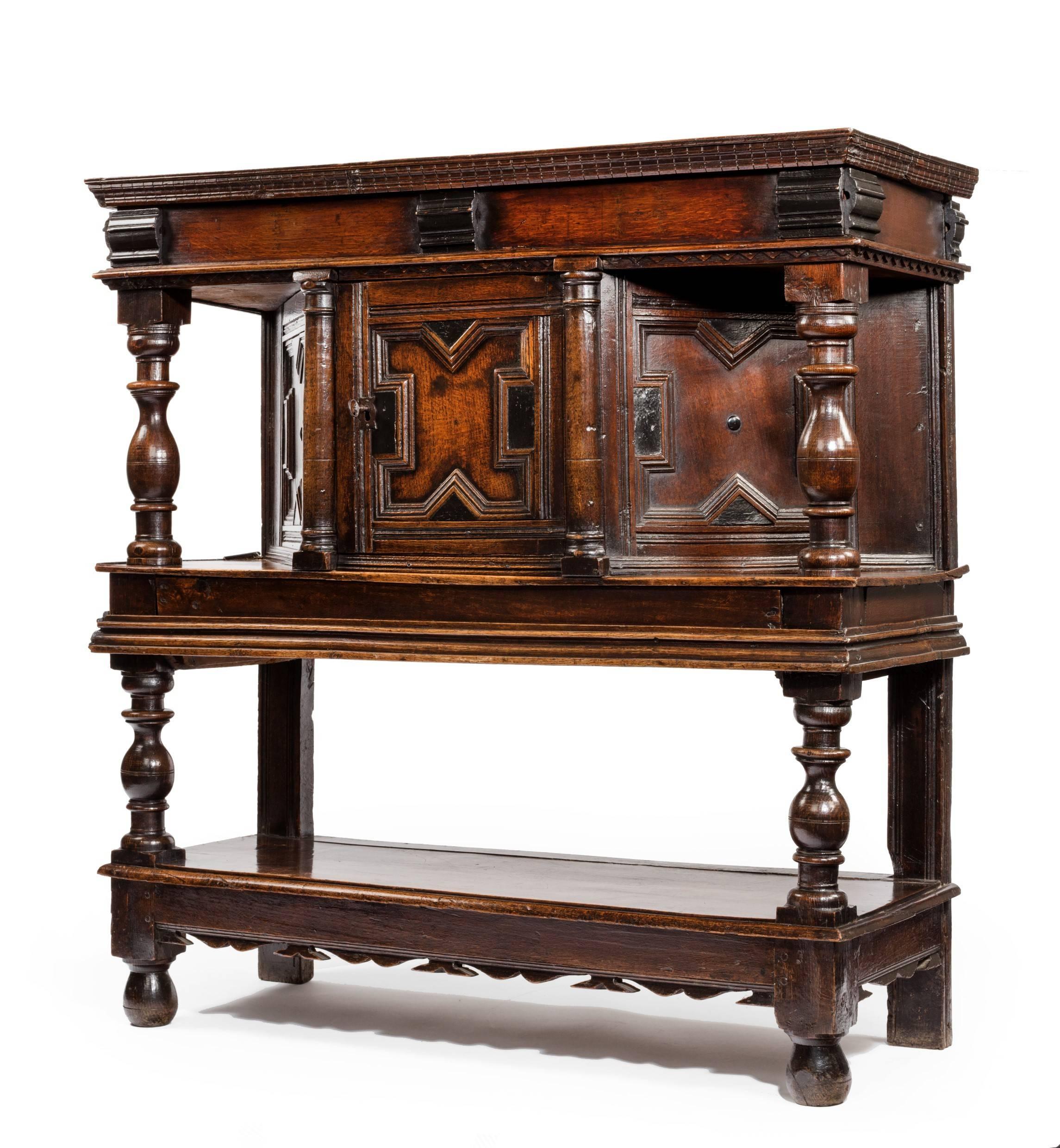 A 17th century oak joined court cupboard made in two sections. The upper part has a secret lift-up lid below the dental type mouldings. The elegant baluster shaped supports geometric moulding with small ebony pieces. Angled side panels and central