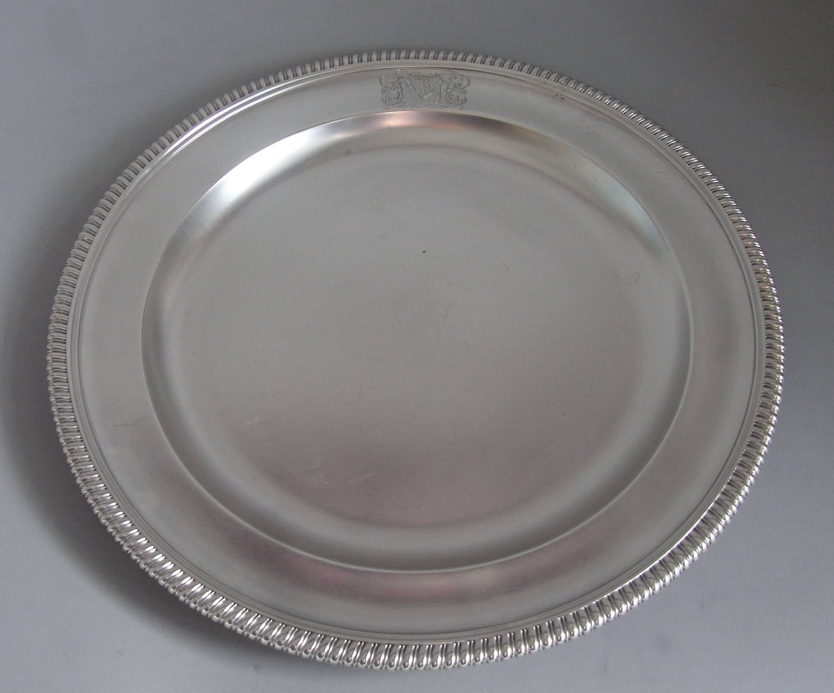The dishes are circular in form with a raised rim which is decorated with a plain gadrooned band. The border is engraved with a contemporary Armorial surrounded by a cartouche of drapery mantling, which was a typical design at this date. The dishes