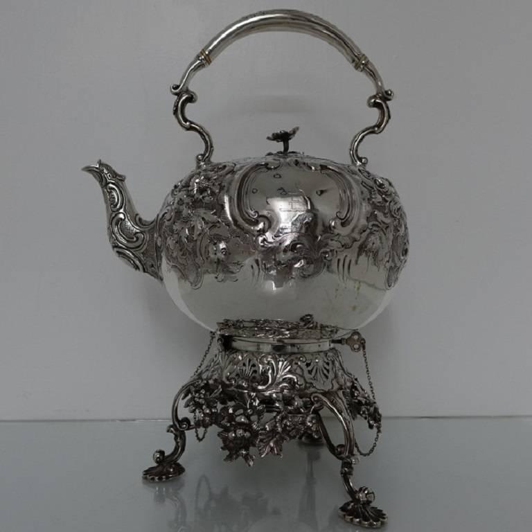 A stunningly beautiful large 19th century Victorian tea kettle on stand with floral and foliate chasing set on a matte background. The kettle has a double cartouche in which sits a family coat of arms and a elegant crest for importance. The lid of