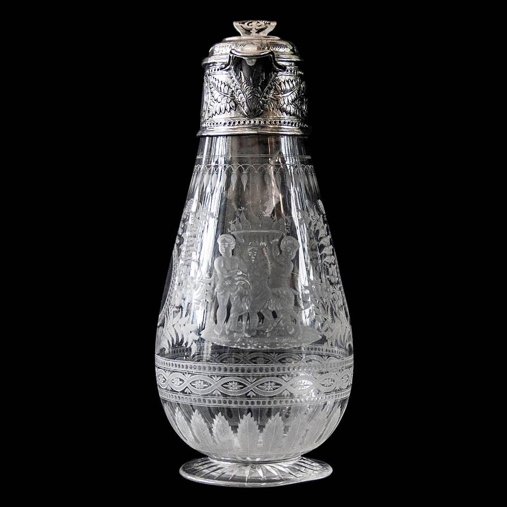 A Victorian glass and silver mounted claret jug on circular star cut foot. The glass body beautifully acid etched with floral decoration with a front panel depicting cherubs bearing fruit. 
The silver mount chased with complimentary floral
