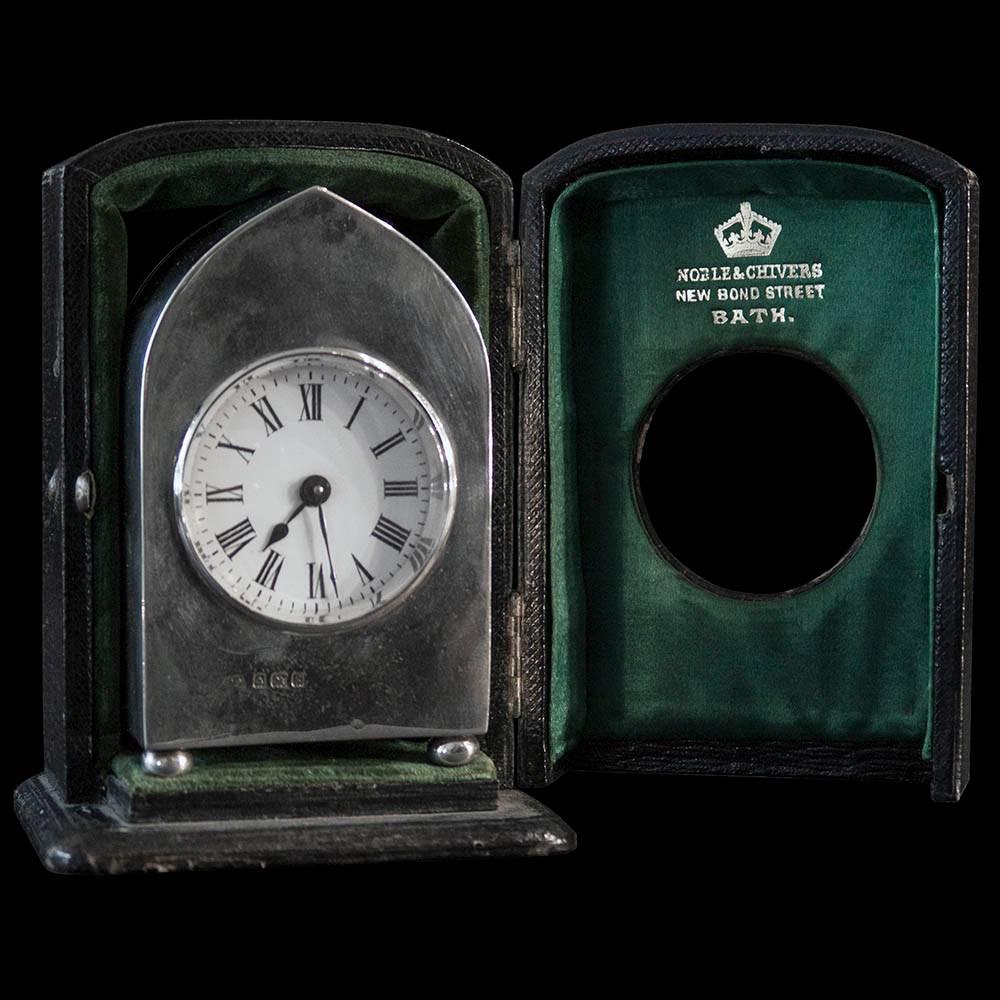 An Edwardian silver cased carriage clock with French movement. The arched plain silver case with hinged door engraved with twin family crest, standing on four button feet all housed in leather bound display or travelling case.