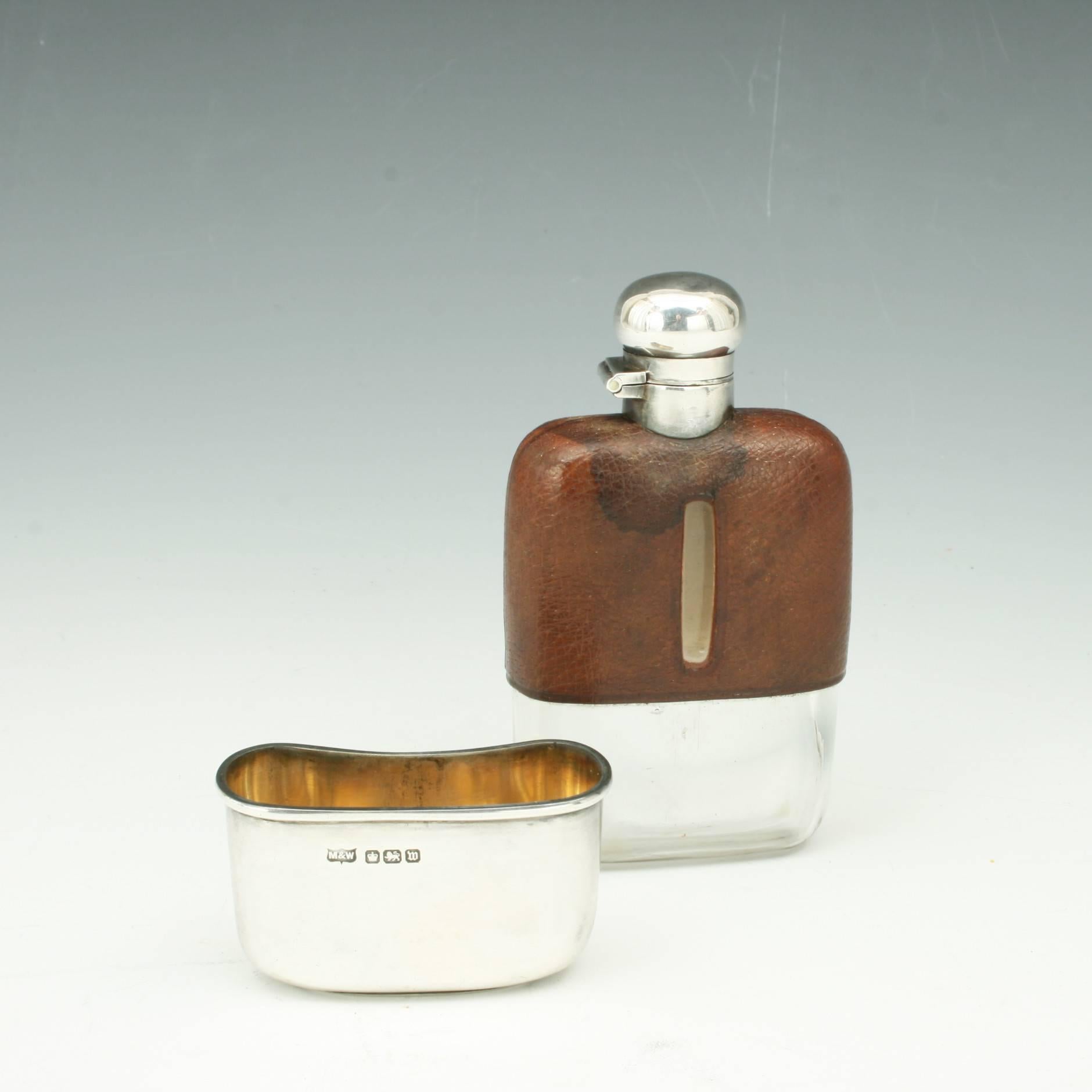 A very nice silver spirit hip flask with the top half covered in leather with level viewing windows cut into both sides. The flask with hinged lid with screw bayonet fitting, bottom with a removable silver drinking cup. Both pieces carry the mark 'M