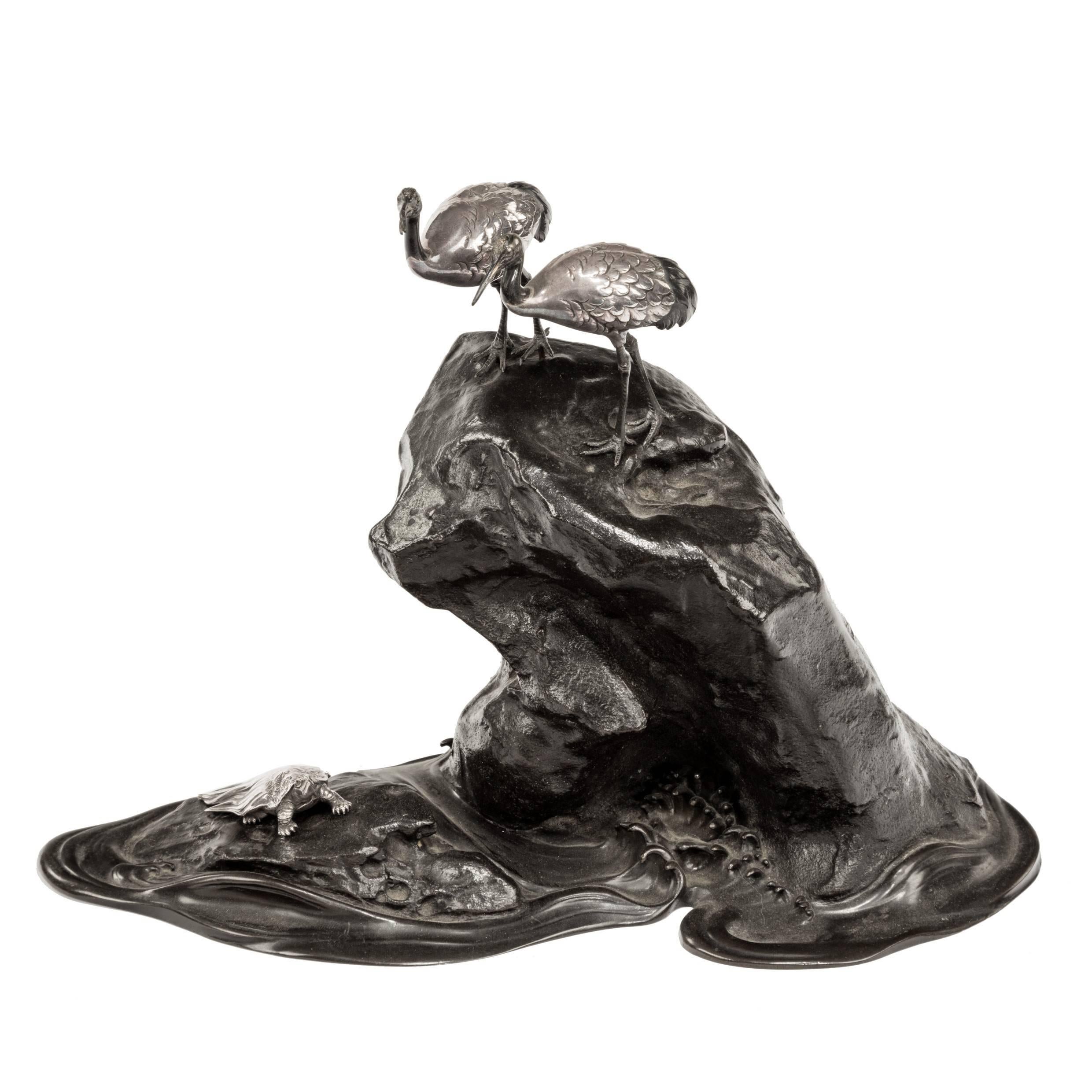 Meiji period bronze okimono of a large rock with two detached silver cranes perched upon it and a detached silver minogame in the rocky pools below. 

Footnote: 
Both minogame and cranes are auspicious creatures in Japanese lore as they symbolize