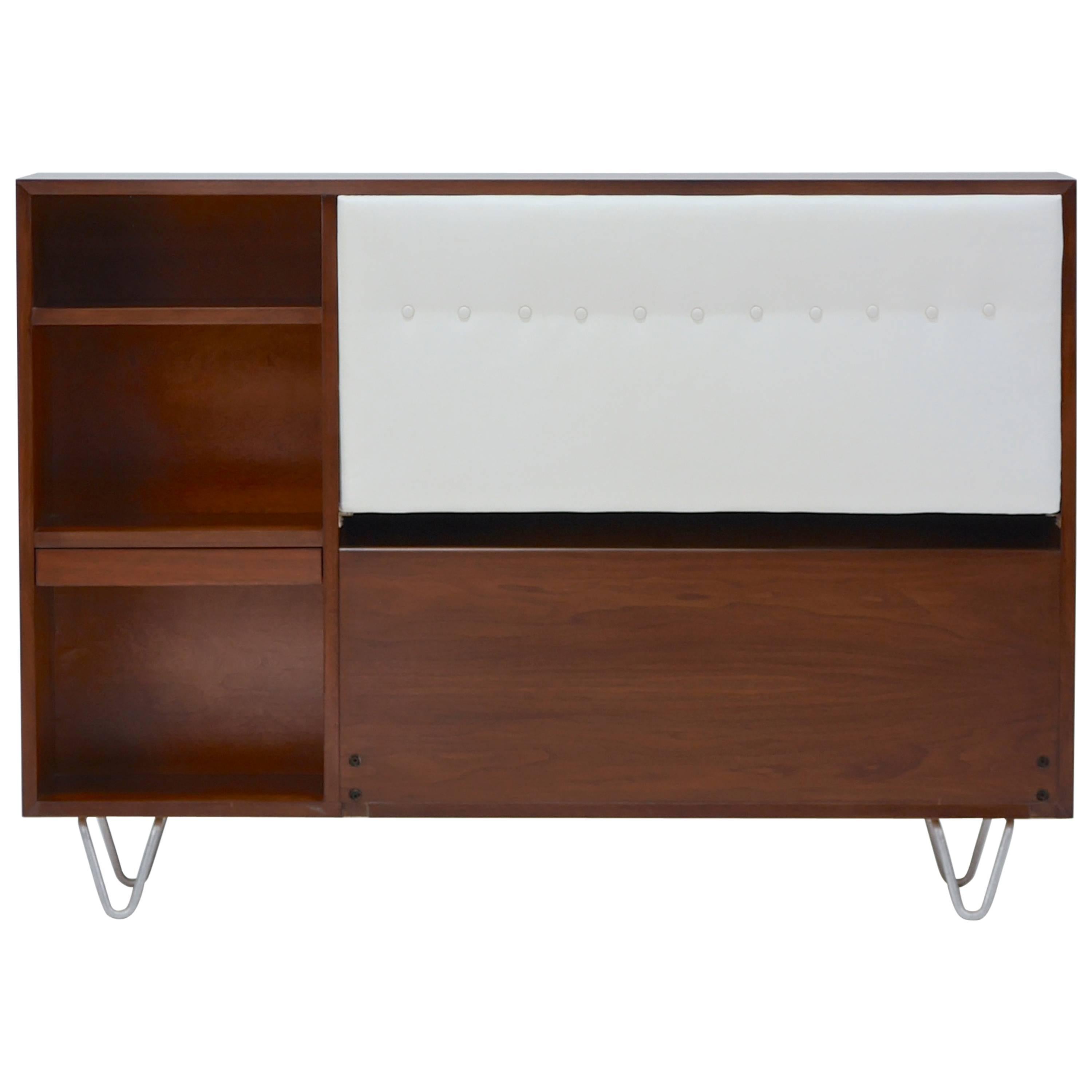 King-size headboard in walnut on hairpin legs by George Nelson for Herman Miller. Recent professional restoration. Features two adjustable pull-out shelves for convenience. The top can be opened and offers storage space for additional bedding,