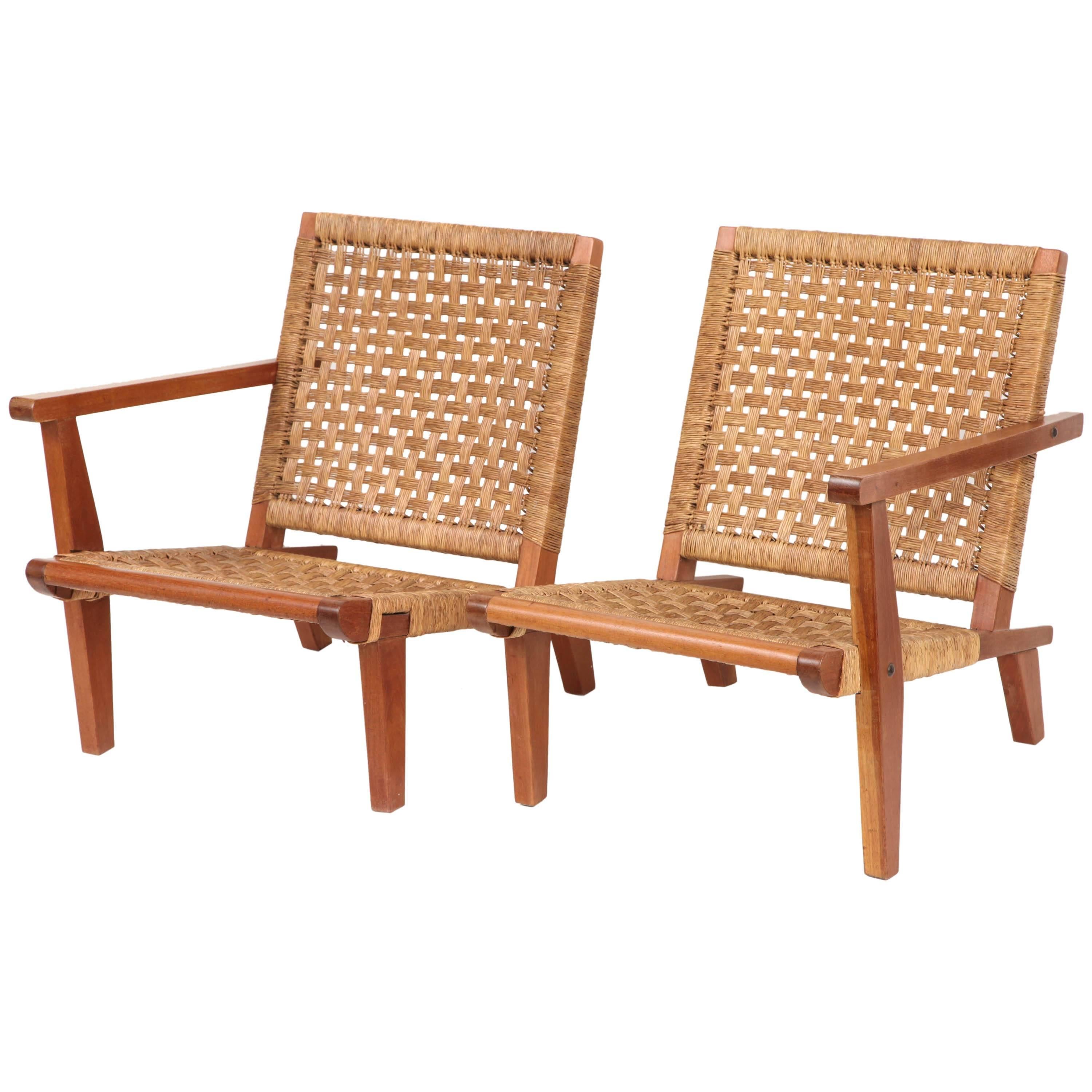 Divided settee by Mexican designer Clara Porset. Bold modernist walnut frames with handwoven rush seats and backs. Mirror image one-arm chairs can be used separately or places side-by-side as a settee. Mexico, 1950s, with original rushing and oiled