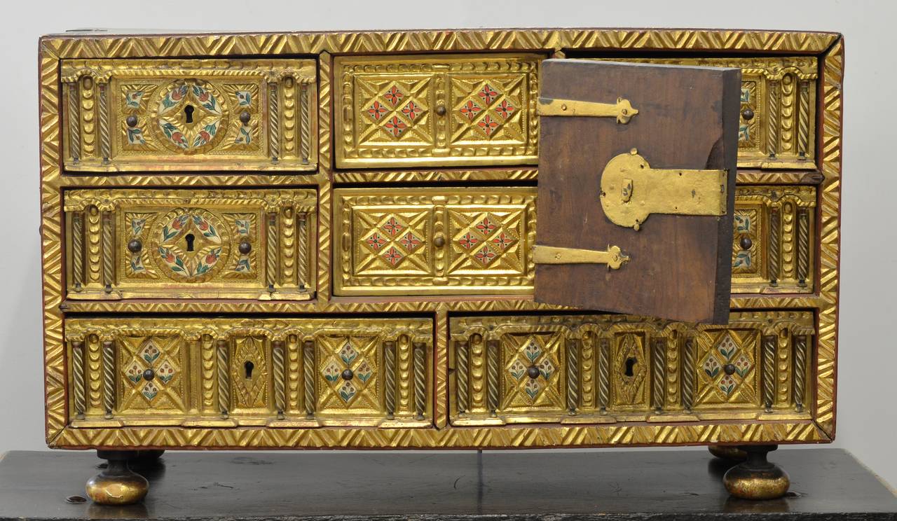 Papillero vargueno (table cabinet), the walnut carcase with gilded cross hatched front borders, the sides with iron carrying handles and decorative iron brackets, the interior gilded and fitted with four drawers either side of a door above two long