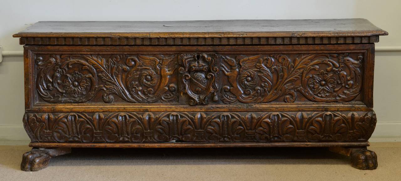 Walnut cassone (coffer) with rising top, the front panel profusely carved in low relief with winged griffons and scrolling foliage either side of an applied coat of arms carved in high relief above a bombé panel carved with a border of stylised