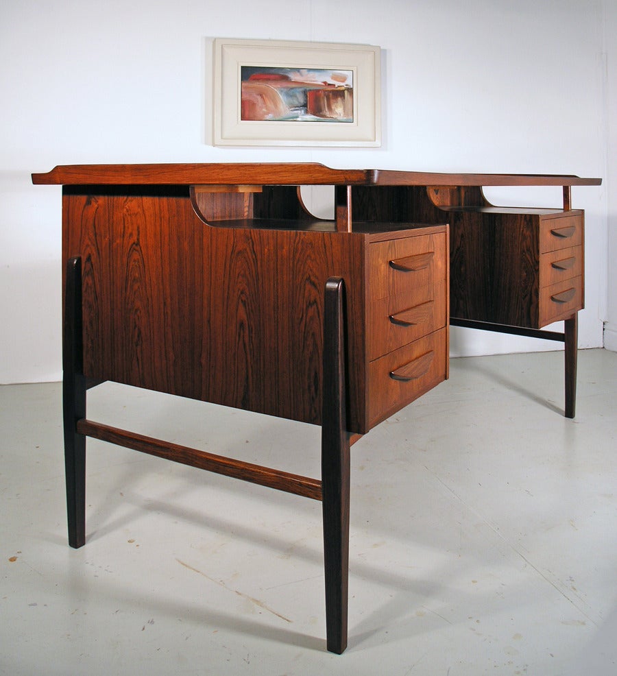 A striking rosewood desk designed by Svend Aage Madsen for Uldum Mobelfabrik.  This has been fully repolished. 6 drawers to front, and two drop down cupboards and bookshelf to back.  Curved top with raised edges.