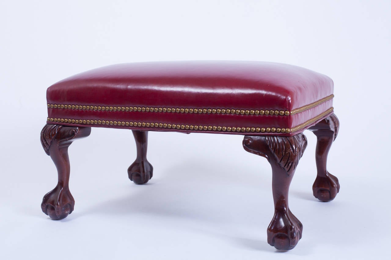This rich red leather ottoman has ball and claw feet and was made in Hickory, NC by Hancock and Moore. It has minor surface scrathes consistent with age, but nothing that a good polish wouldn't alleviate.
