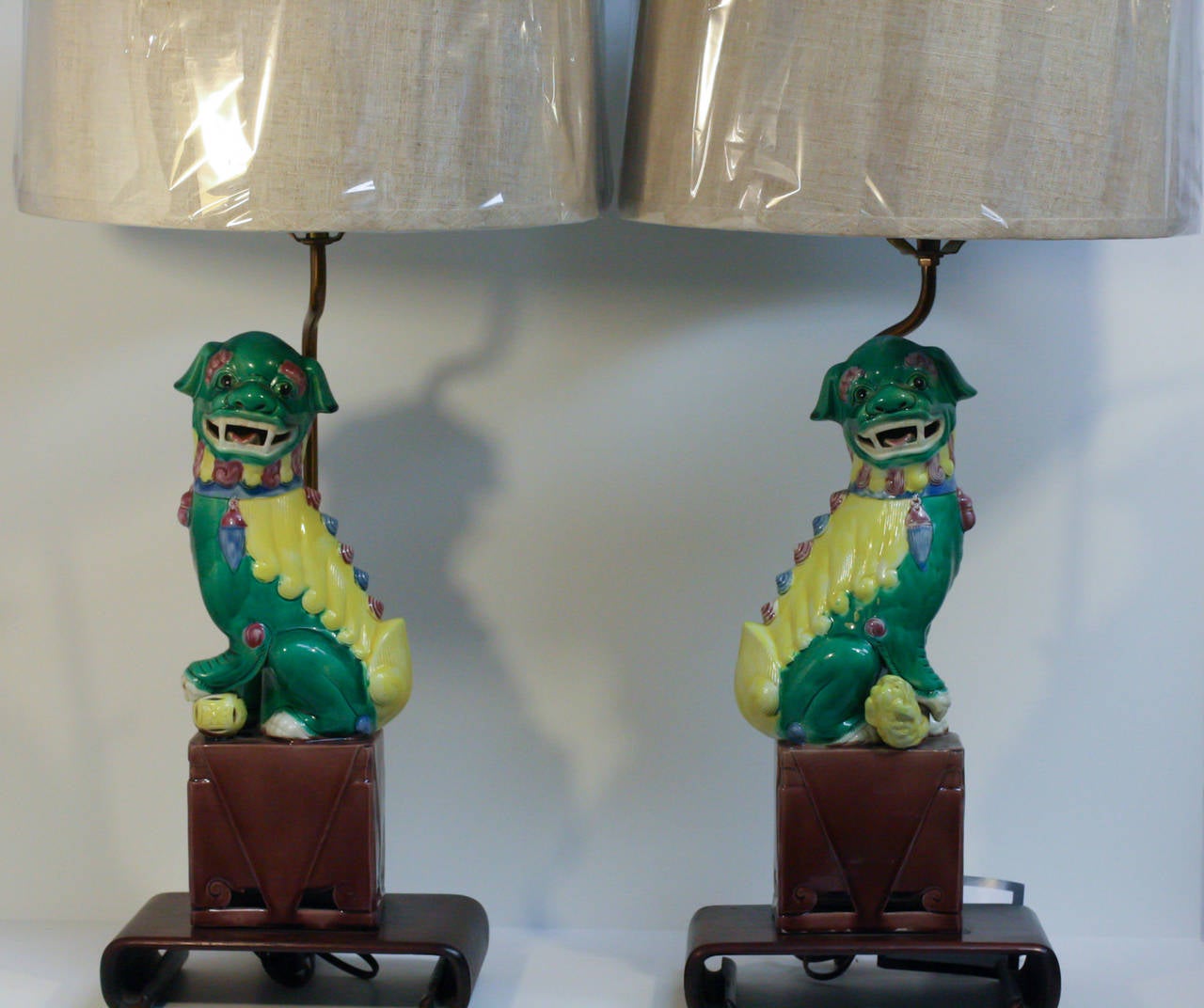 These handsome porcelain foo dog lamps are multicolored featuring green, yellow, blue and bown. Thet are perched on a ming style stand.