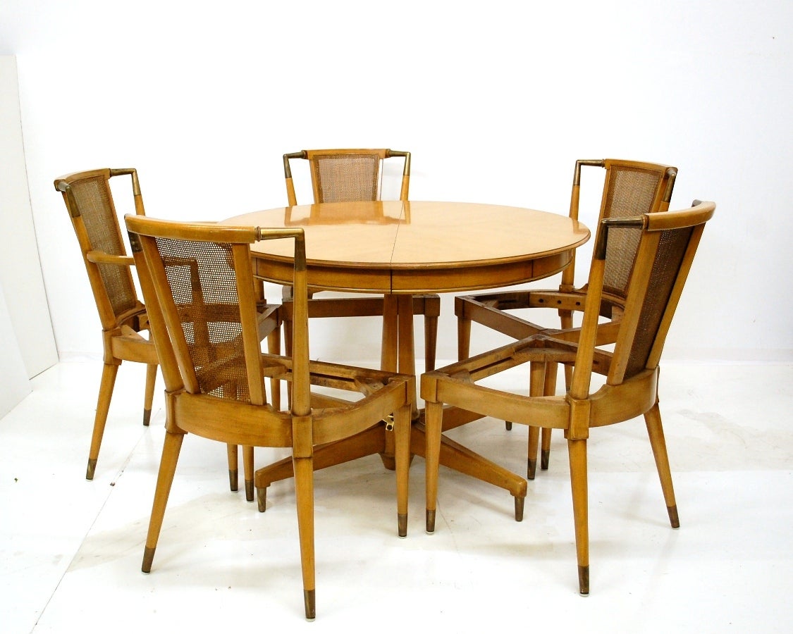This set of six elegant chairs, two with arms, is crafted with a curved caned back and brass trim at the corners  and feet.  The chairs are newly upholstered in an olive/khaki color.  The table is 42 inches in diameter and has two 14 inch leaves,