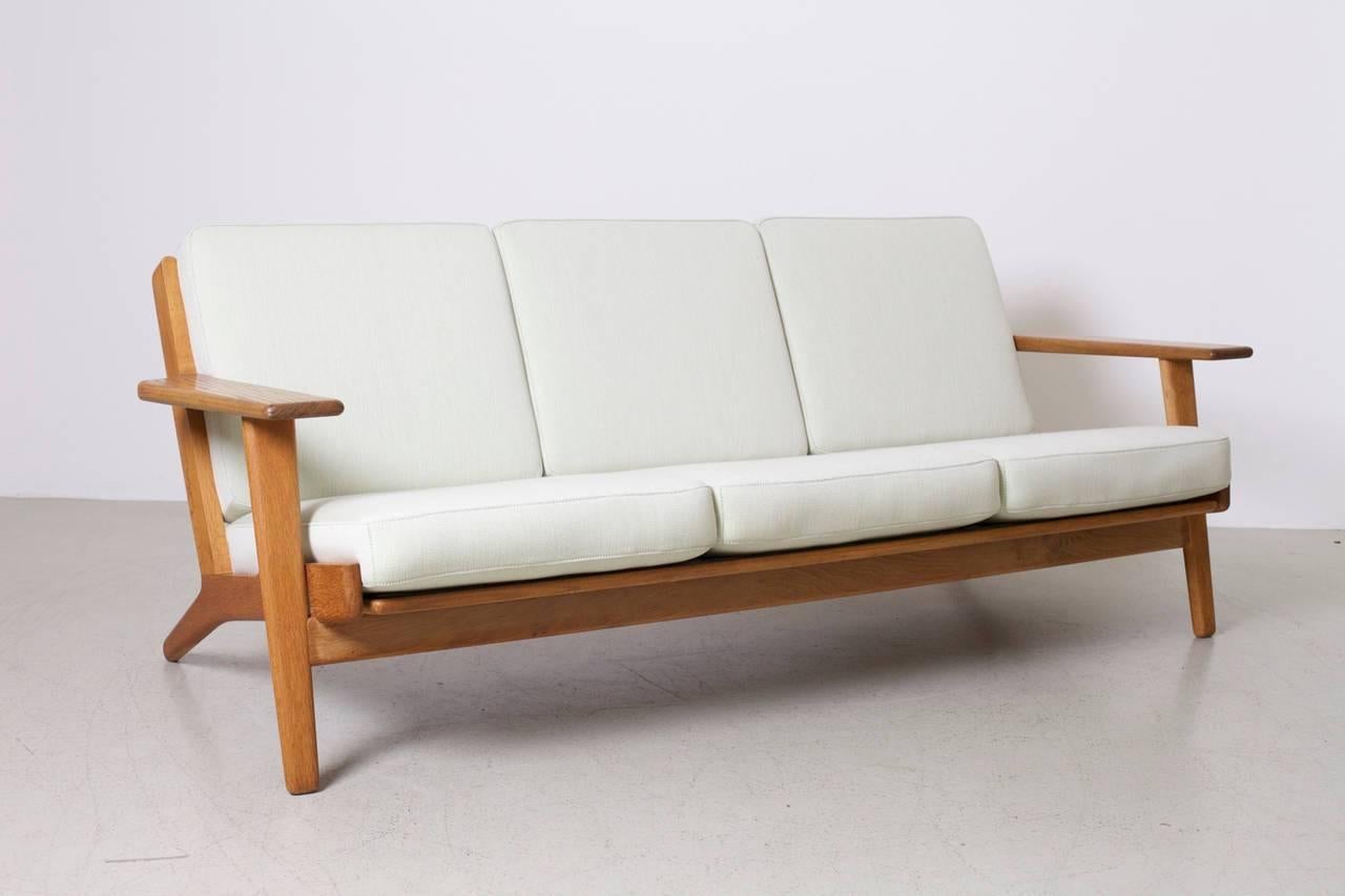 Hans Wegner GE 290 sofa for GETAMA, Denmark in solid oak with original pillows. New covered in Fanny Aronsen Balder very light green fabric.

