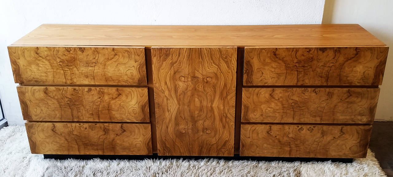A stunning piece of furniture-- a 1970s Milo Baughman olive burl wood credenza, dresser or chest with a fabulous ebonized base. This piece is a gorgeous piece of furniture that is quite substantial and sure to compliment any Mid-Century Modern or