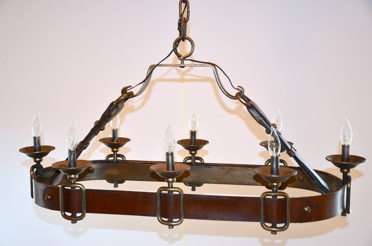 In the style of Jacques Adnet or Hermes. Iron and saddle leather eight-light chandelier, newly rewired. Heavy iron chain and hammered canopy.