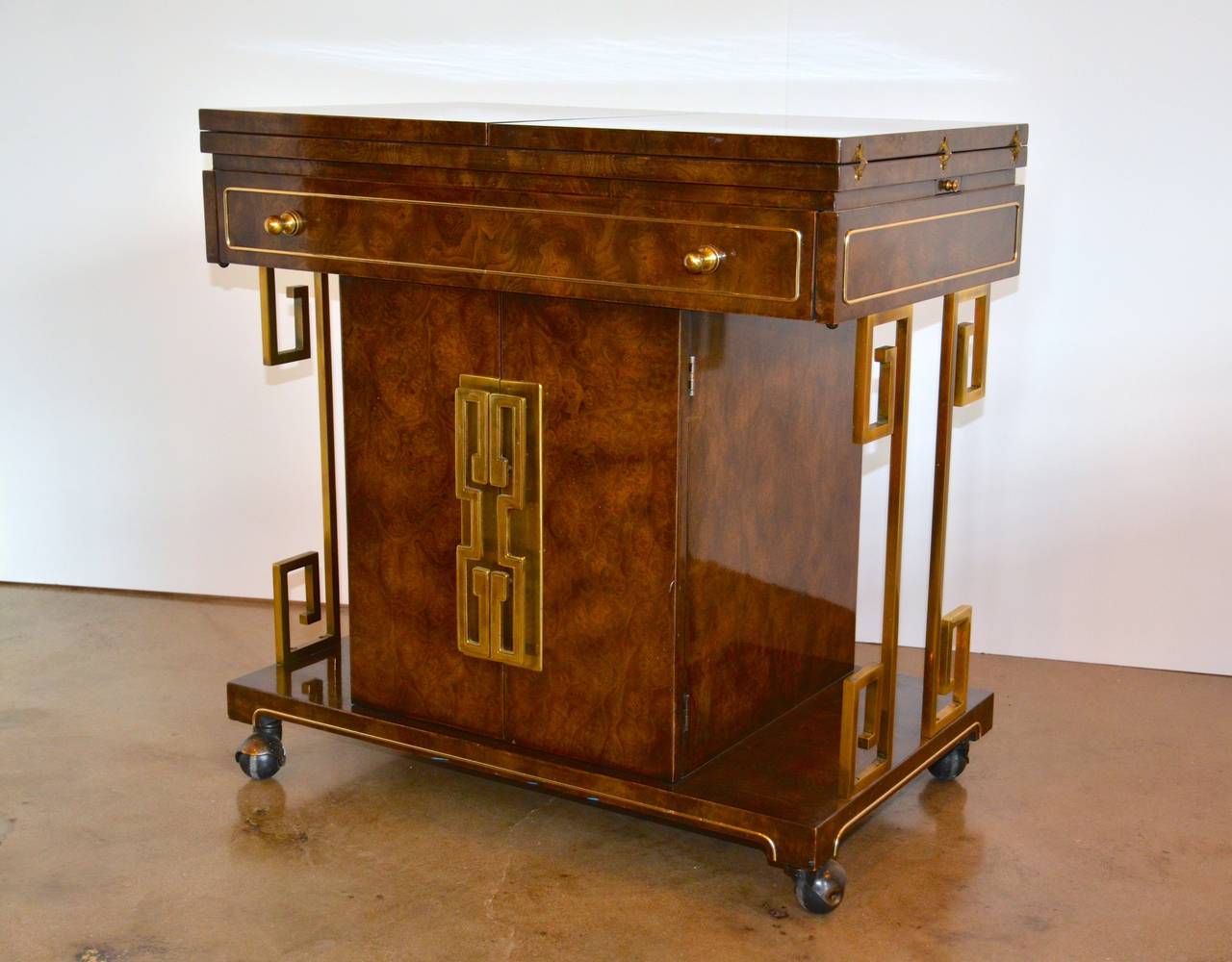 Bernhard Rohne's rolling bar cart from Mastercraft features a beautiful burled amboyna wood finish and brass Greek key side supports. The two-piece top flips out from the middle to reveal a 5' laminate service deck. There is ample storage for