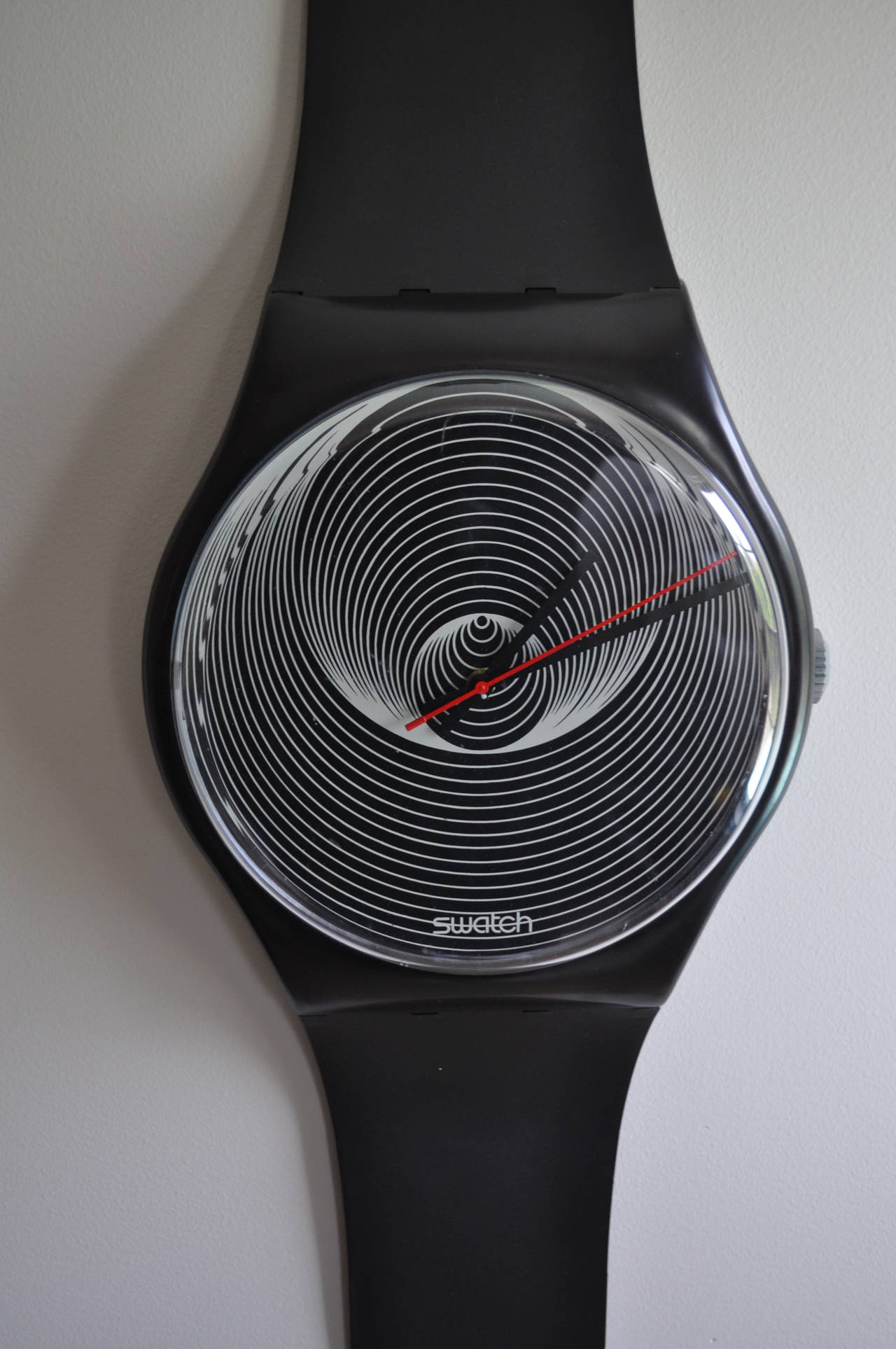 Iconic 1980's Swatch Watch Pop Art Wall Clock.  This wall mounted sculptural piece features a unique psychedelic black and white swirl face with a classy black frame and band.  Can be displayed with or without the included original clear face case. 