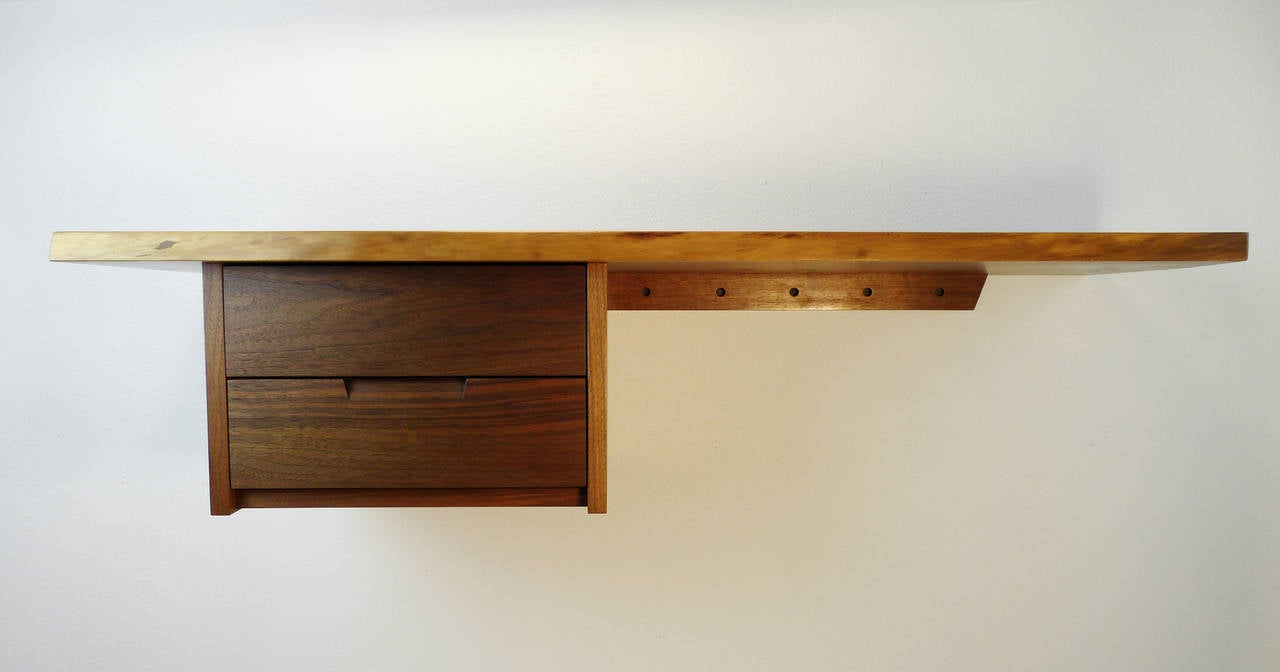 This is a wall-mounted walnut desk by Mira Nakashima, daughter of famed Japanese American woodworker George Nakashima. Featuring two stacked drawers and a natural color top with a natural front edge and flat beveled edge at one end. The desk is