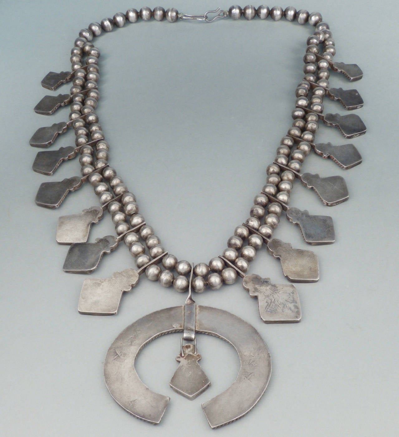 A beautiful and unusual Zuni interpretation of a squash blossom necklace, this piece features channel inlaid natural green turquoise with a very modernist layout. Handmade beads.
20 1/4