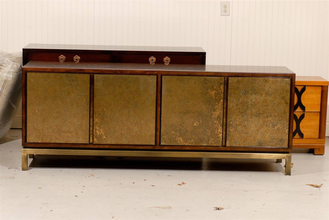 An absolutely stunning buffet or credenza by John Widdicomb, circa 1970. Handsome burl walnut case construction, atop a solid brass base. Fabulous reverse painted glass doors highlight the piece. This stout and expertly made piece will serve as