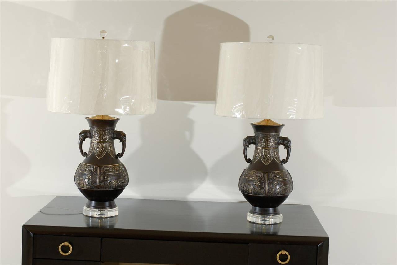A striking pair cast urn lamps.  Solid brass with beautiful relief and detail with solid brass accents.  Bronze finish applied and then distressed, revealing brass highlights hidden beneath.  Elephant heads mark the neck for drama and good luck. 