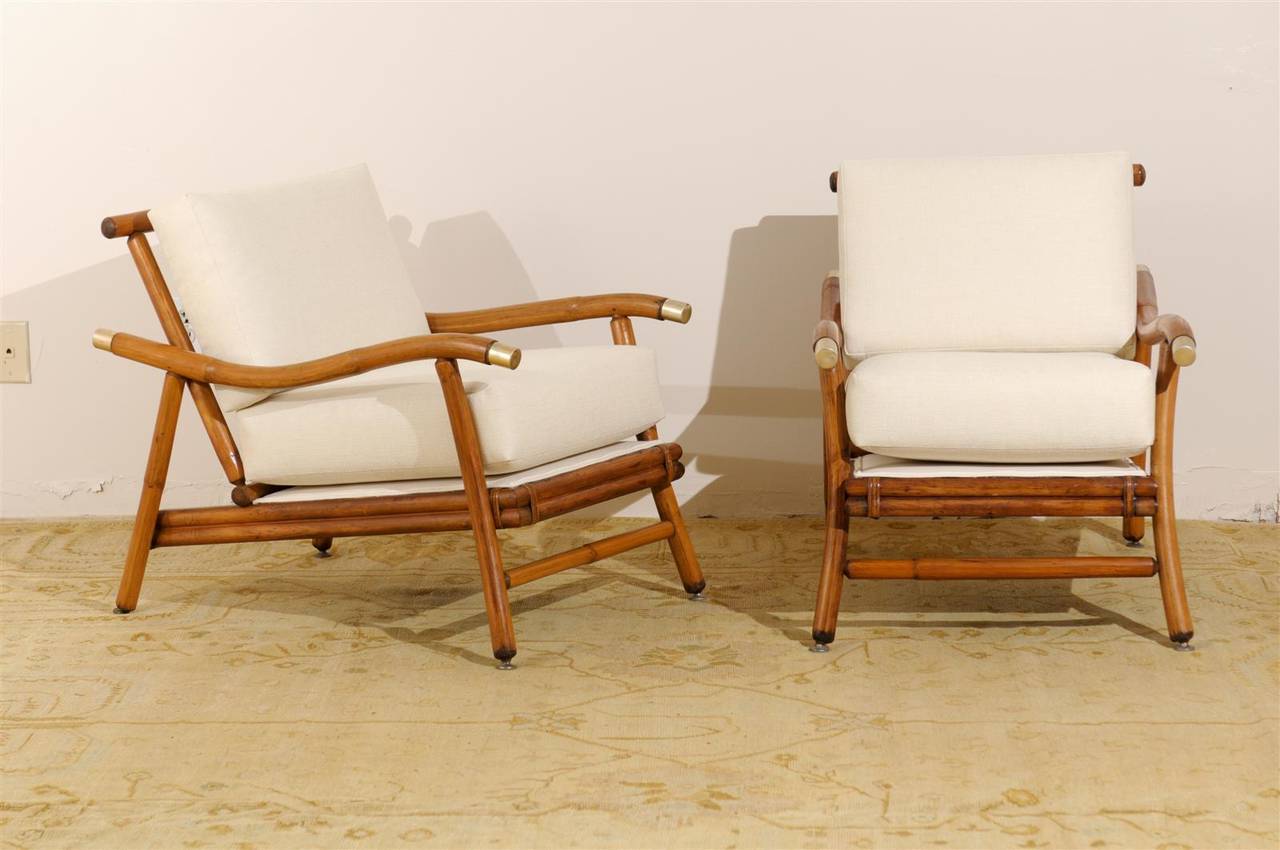 A beautiful and rare pair of Campaign style lounge chairs. Stout rattan and hardwood frame. Fabulous arm detail with brass accents. Aged to absolute perfection. These unusual chairs were part of the 