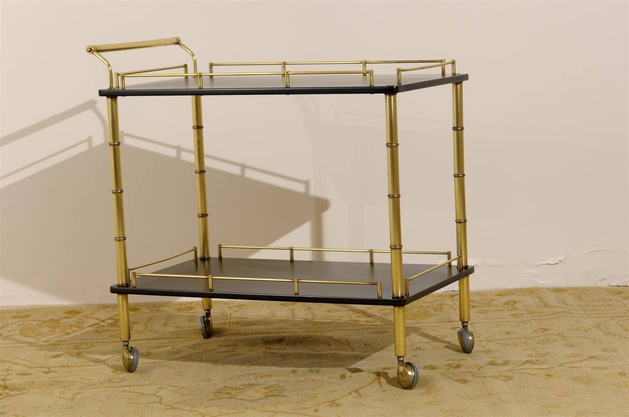 A beautiful vintage Maxwell Phillips bar cart, circa 1970. Solid brass frame with faux-bamboo detail and shelves finished in black lacquer. Atop solid brass casters. Old Money ! Excellent Restored Condition. Shelving is in beautiful condition. The
