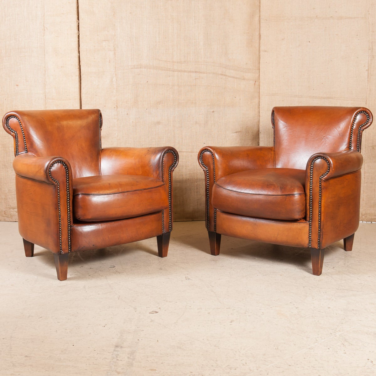 Pair of French Art Deco leather club chairs. Rolled arms and back with nailhead trim. Original leather, professionally reconditioned. The aged patina of these Classic club chairs exudes luxury and character. They are timeless, offering an instant