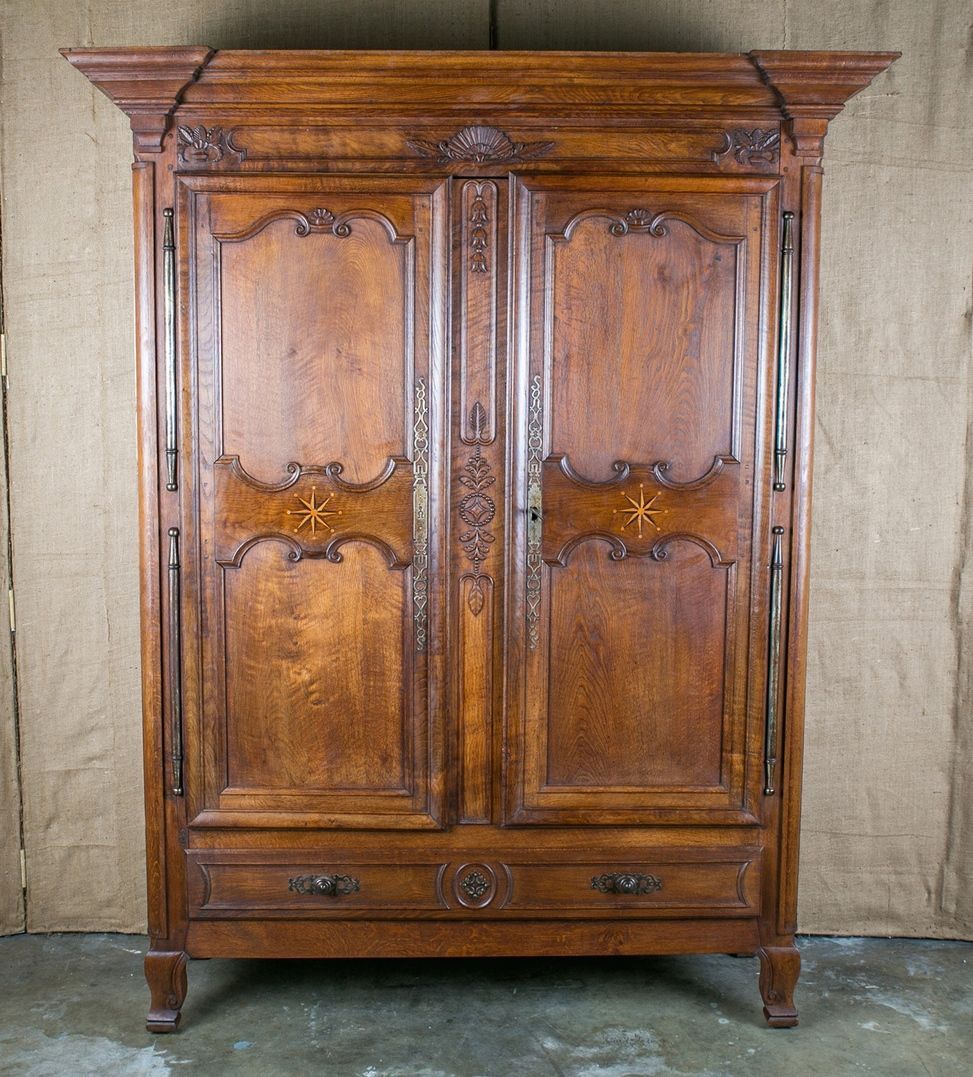 Antique country French armoire handcrafted by the master artisans of Saint-Malo, a port city in Brittany. Stepped cornice with corbels and carved frieze atop half round corner posts that flank two doors with raised center panels featuring inlaid