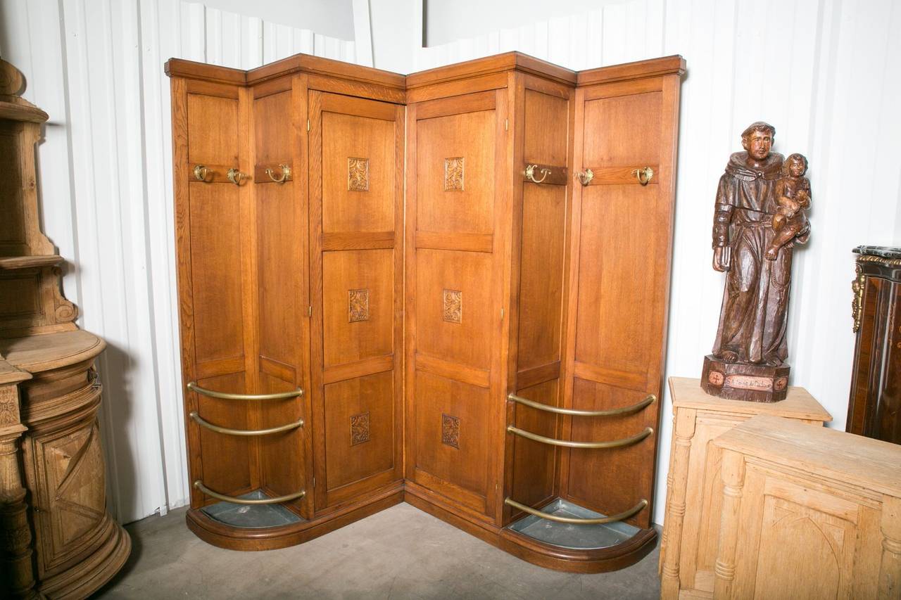 Rare and unusual French Art Deco corner coat closet from a Parisian cafe´. Triple-panel center doors with carvings open to closet area with single shelf and hangers. Each side compartment features an umbrella stand with original brass railing and